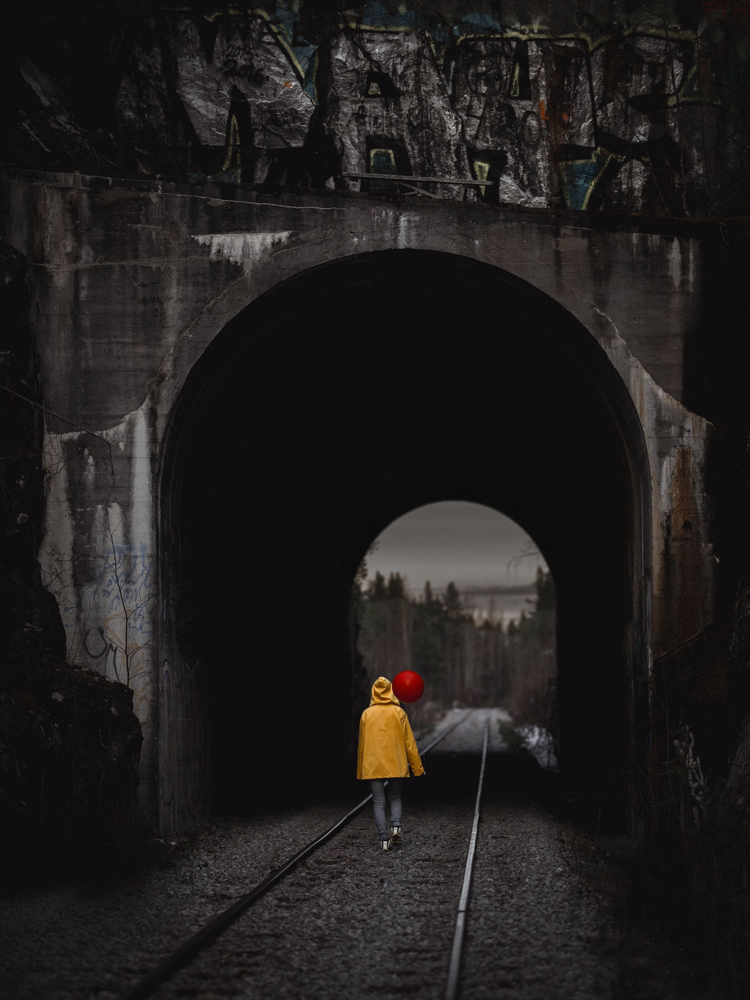 A figure in a yellow raincoat walking through a dark railway tunnel creates a striking contrast in moody lighting.