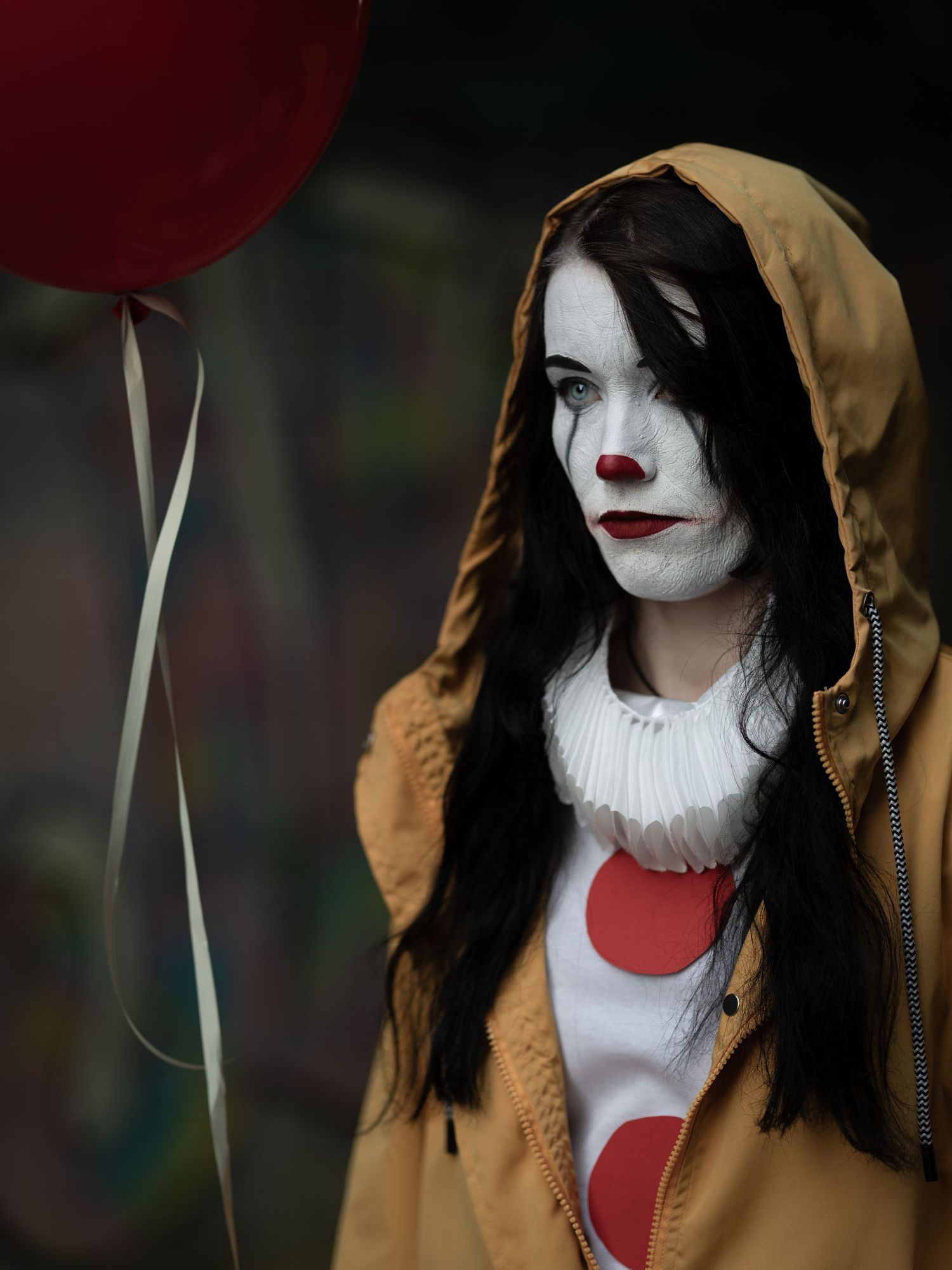 Teatraliskt clownporträtt i gul regnrock med röd ballong och dramatisk belysning.