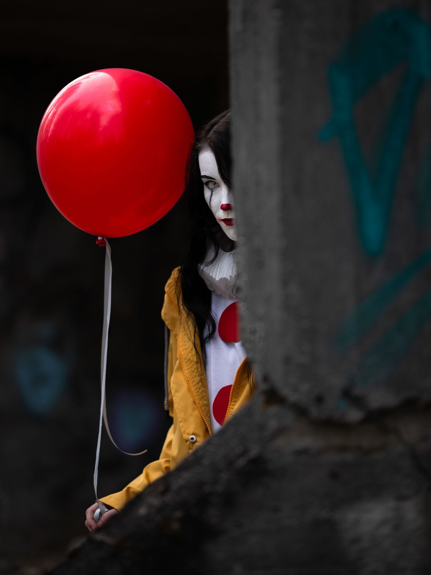 Kuslig clownfigur med röd ballong som kikar fram bakom väggen medan hon bär gul rock.