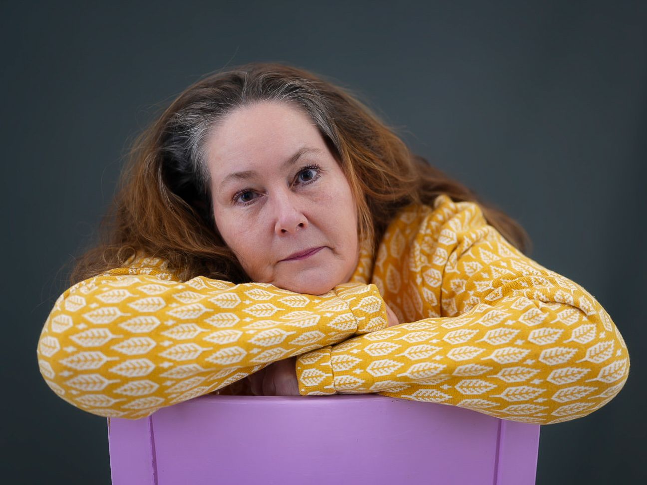 A portrait featuring someone resting on a yellow patterned pillow against a dark background.