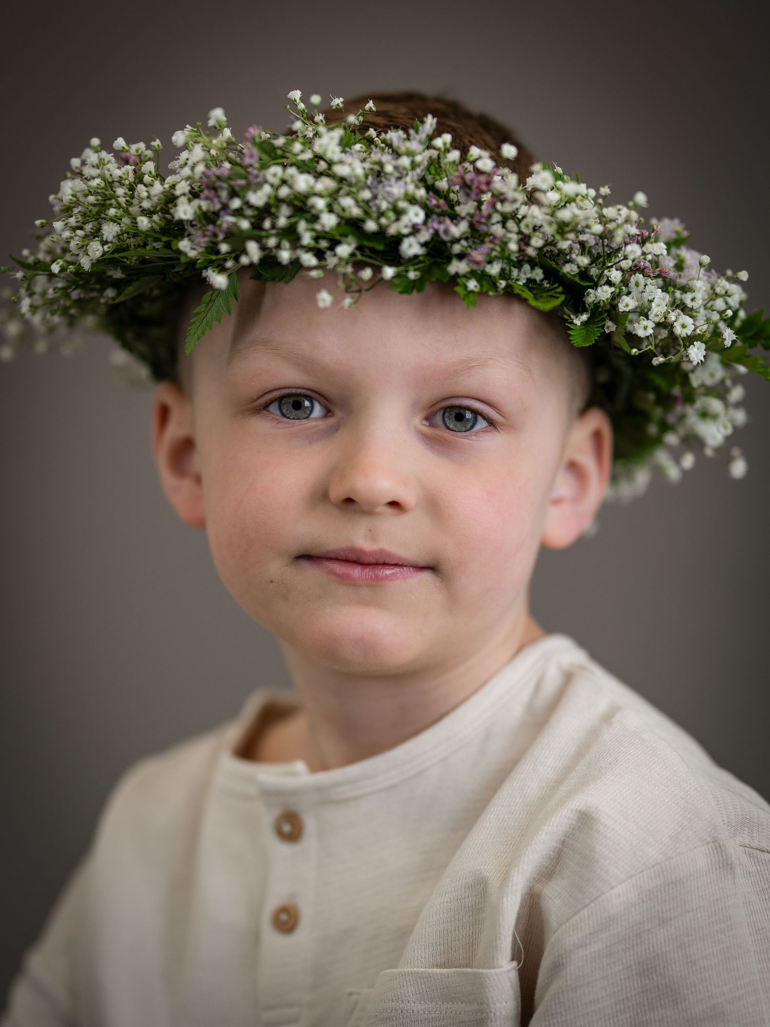Portrait wearing a white crown of baby's breath flowers against a dark background.
