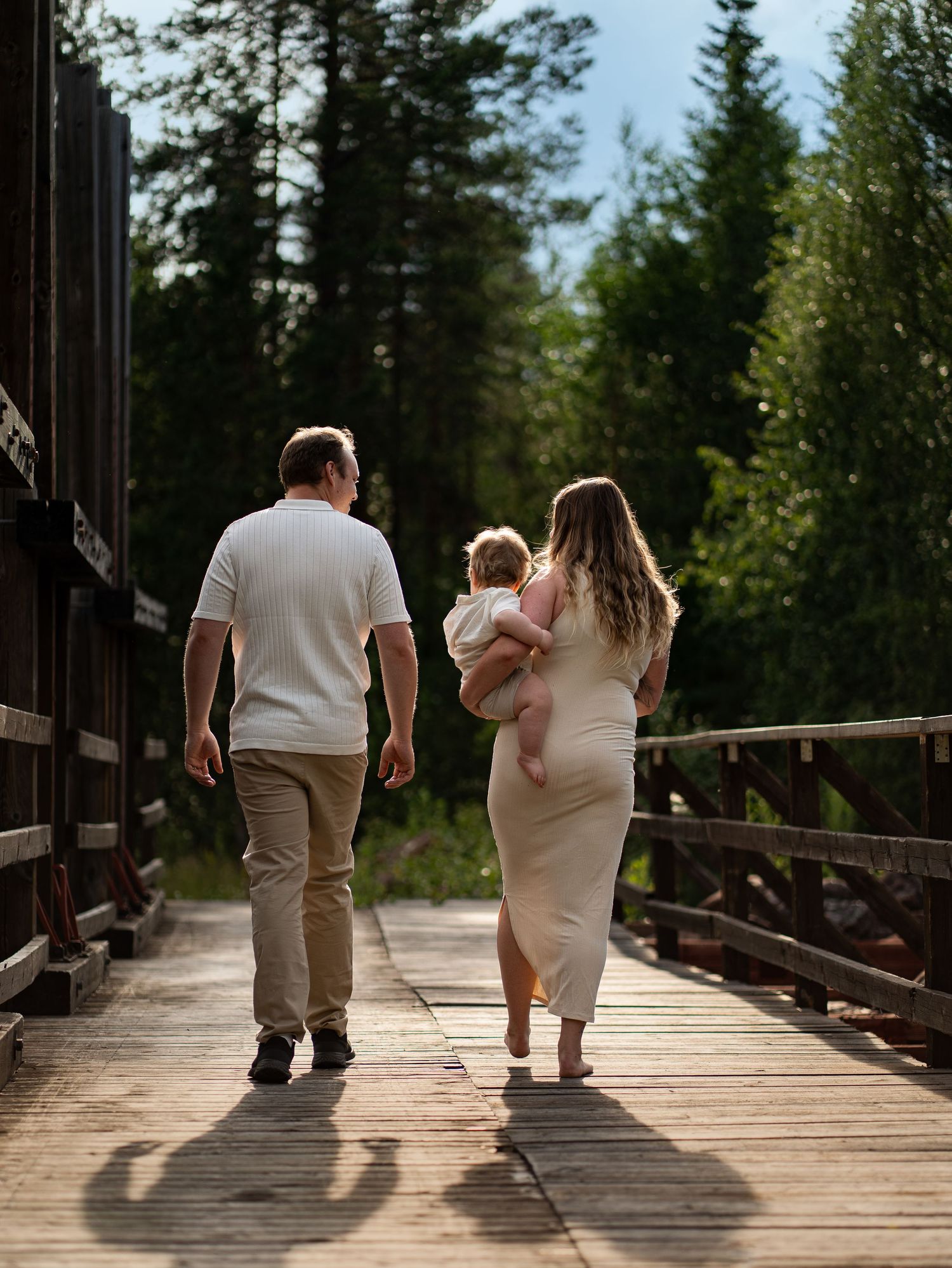 Familj går tillsammans på träbrostig genom skogen.