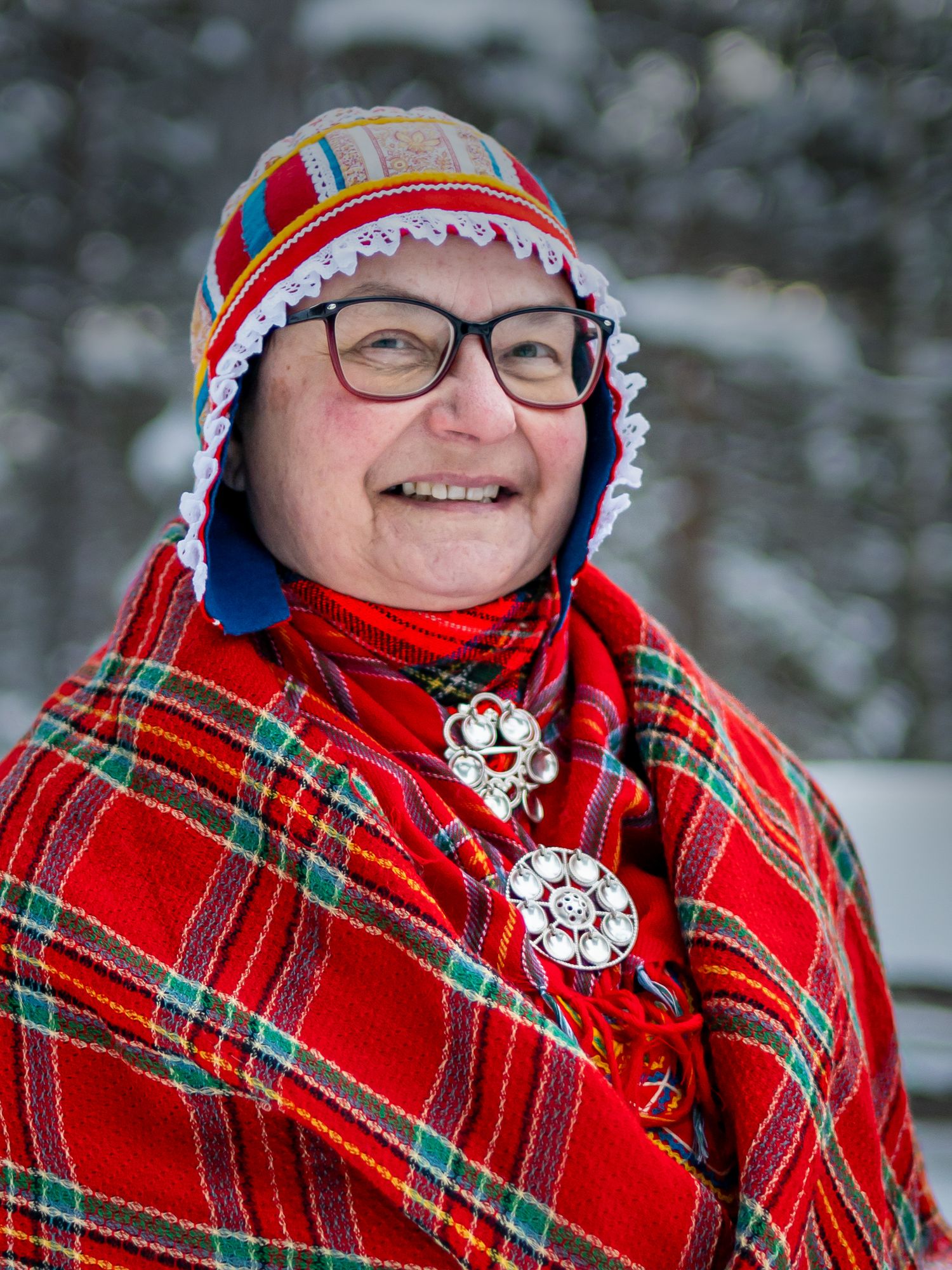 Person som bär festlig röd rutig halsduk och vintermössa ler mot snöig bakgrund.
