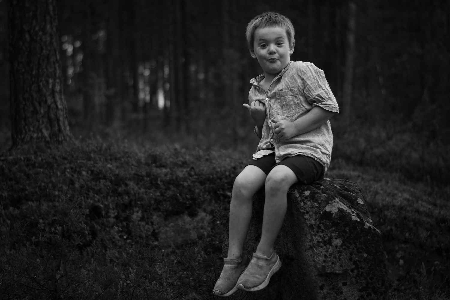 Ett litet barn sitter ensamt på en sten i en stämningsfull svartvit skogsmiljö.