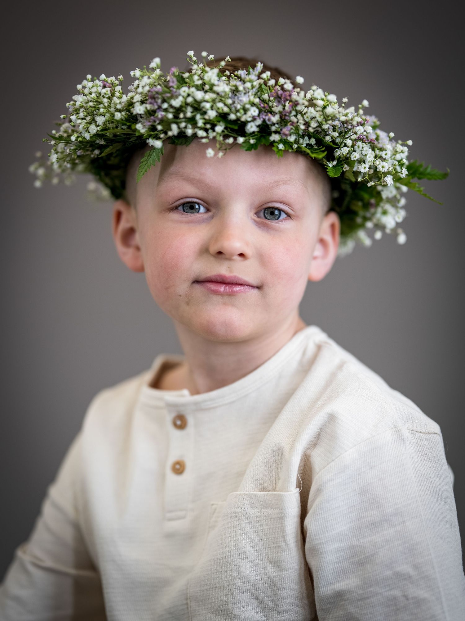 A child wearing a delicate crown of baby's breath flowers and a cream-colored sweater in a studio portrait series.