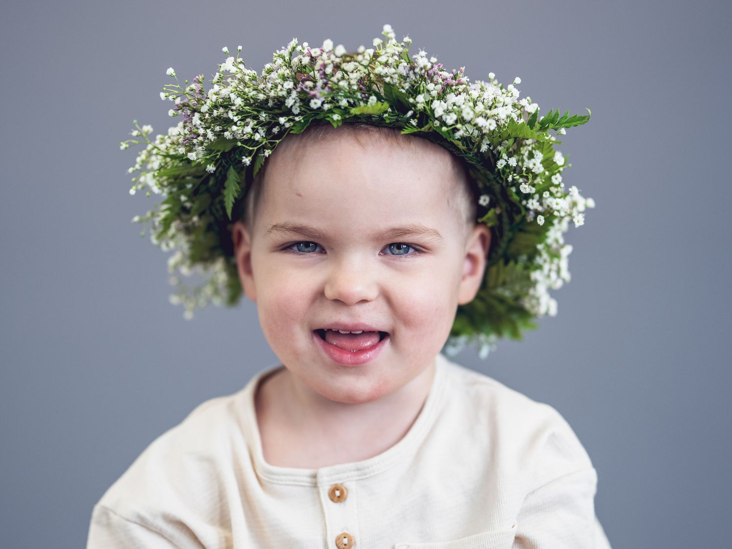 A joyful expression radiates beneath a delicate crown of small white baby's breath flowers against a gray background.