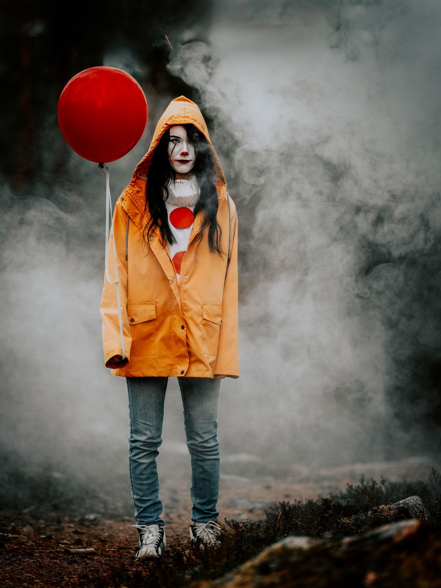Spöklik figur i gul regnrock som håller en röd ballong står i en dimmig skog.