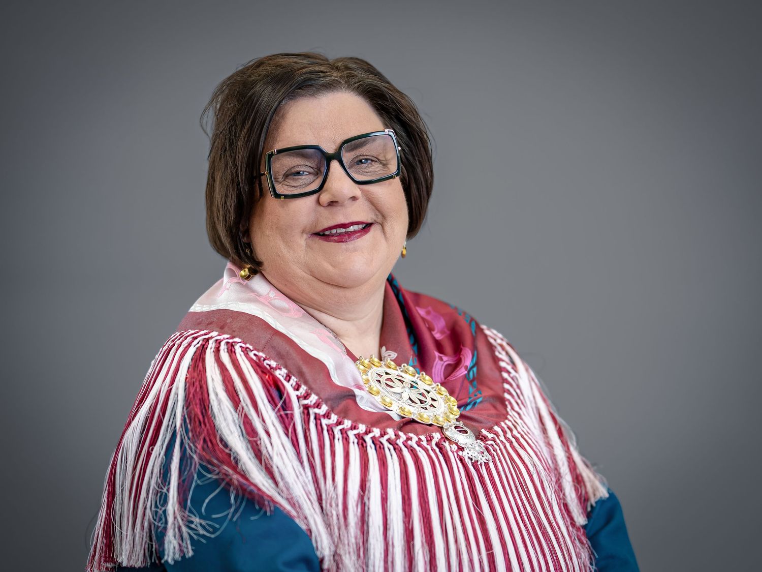 Studio portrait wearing red and white striped traditional dress with decorative jewelry.