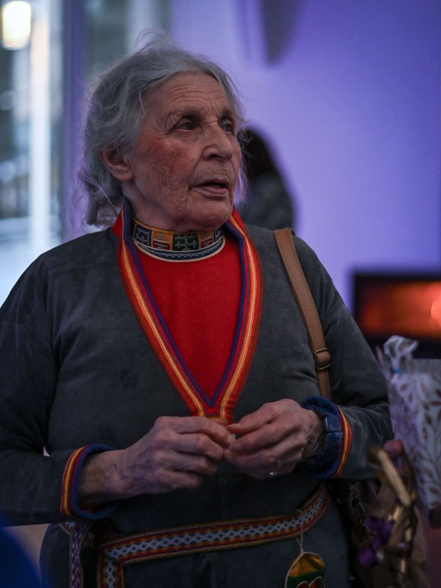 Person i traditionella samiska kläder med färgglada broderade detaljer mot lila bakgrund.