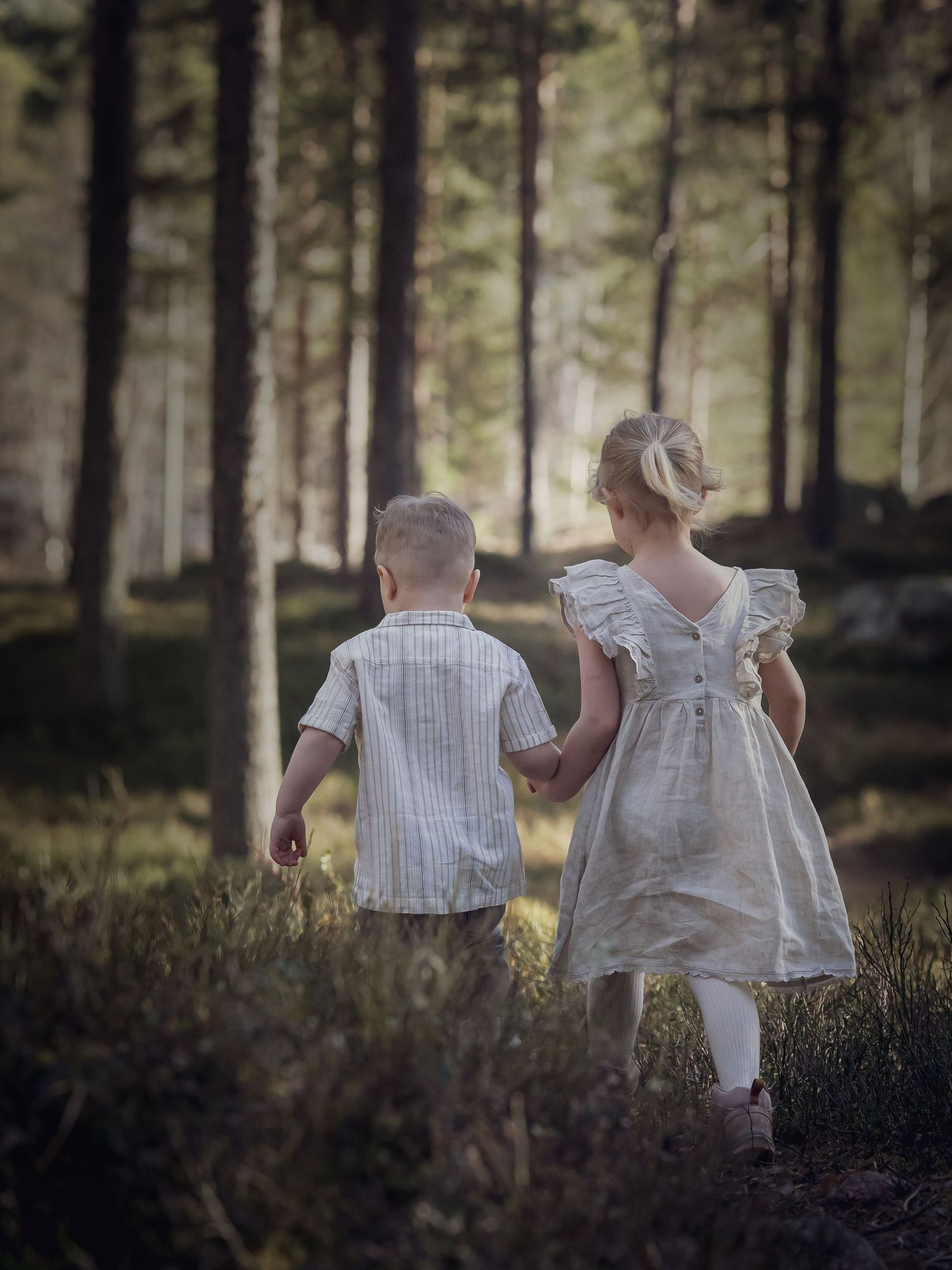 Children in white vintage clothing walk through a misty forest setting.