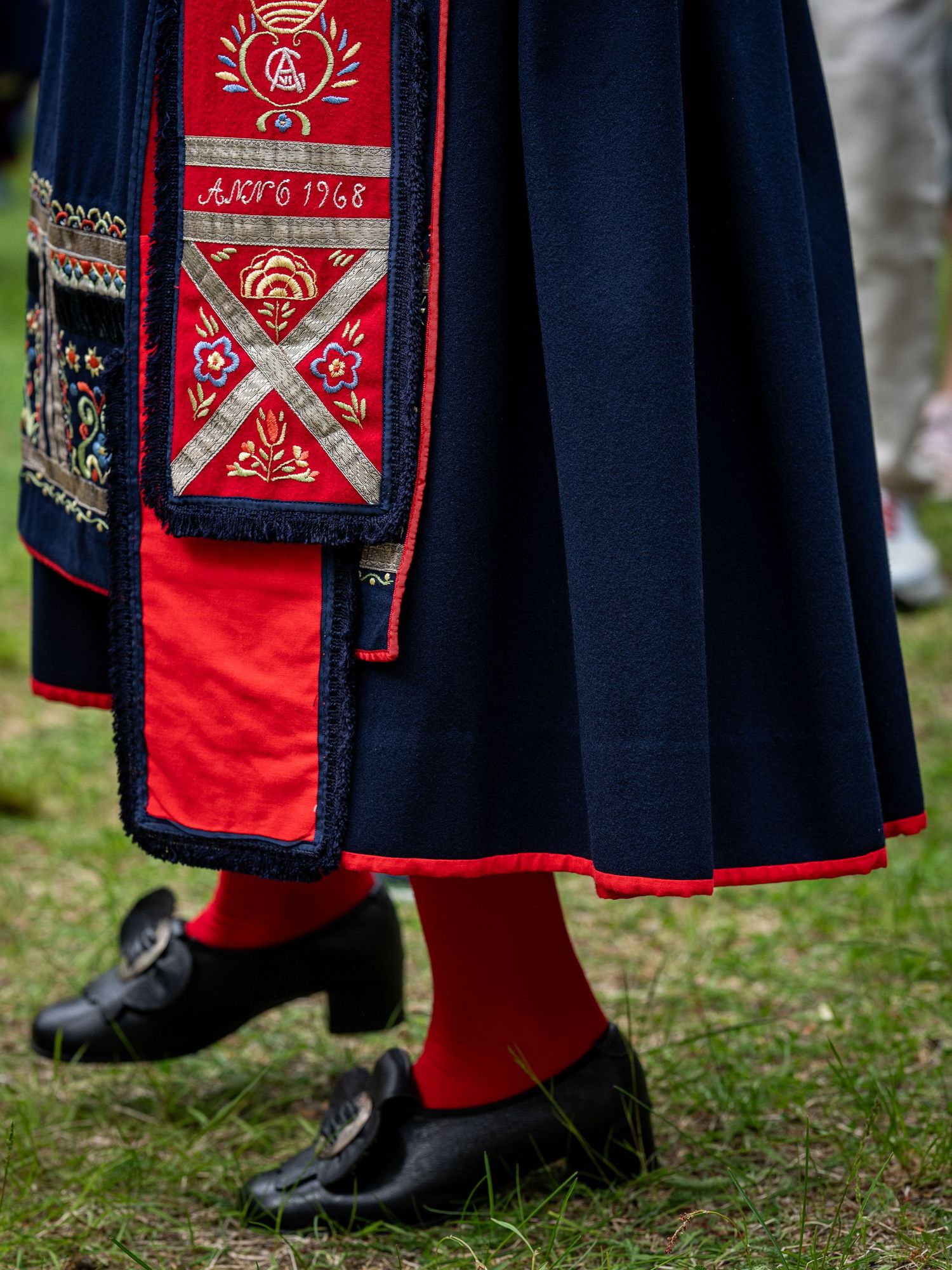 Traditional Norwegian folk costume detail showing navy blue skirt with red trim and black leather shoes with red socks.