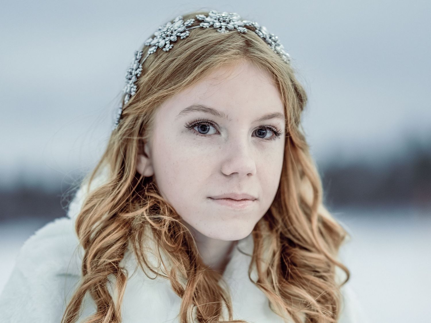 Winter portrait with crystal hair accessories and wavy blonde hair against snowy background.