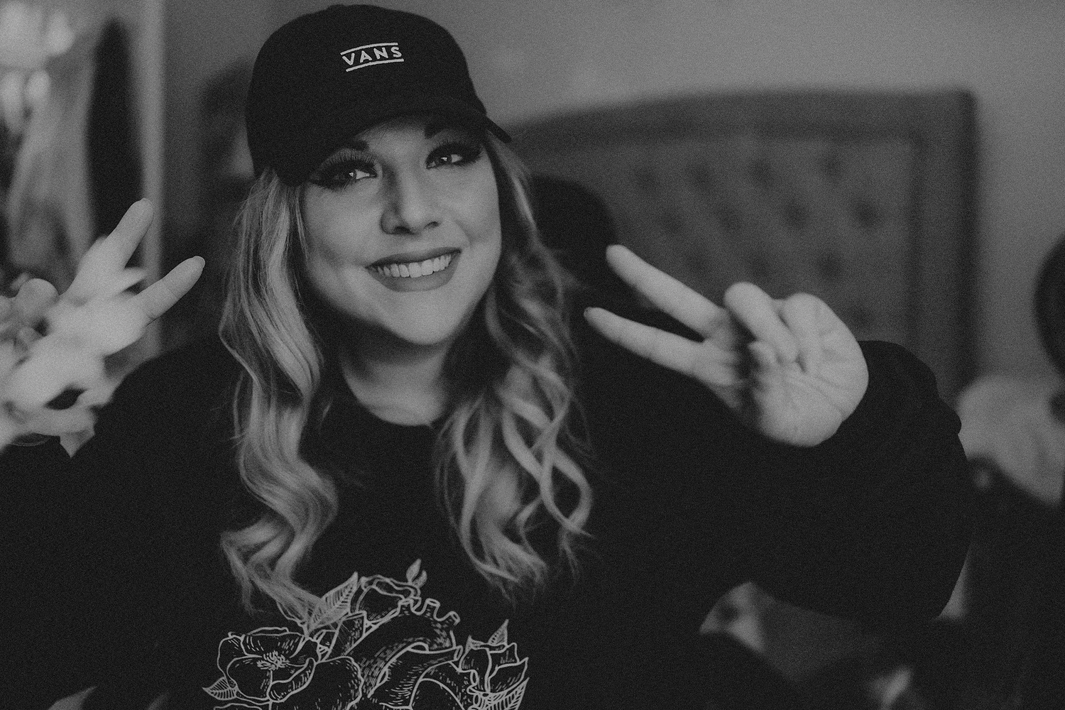 Black and white portrait of person wearing baseball cap making peace signs.