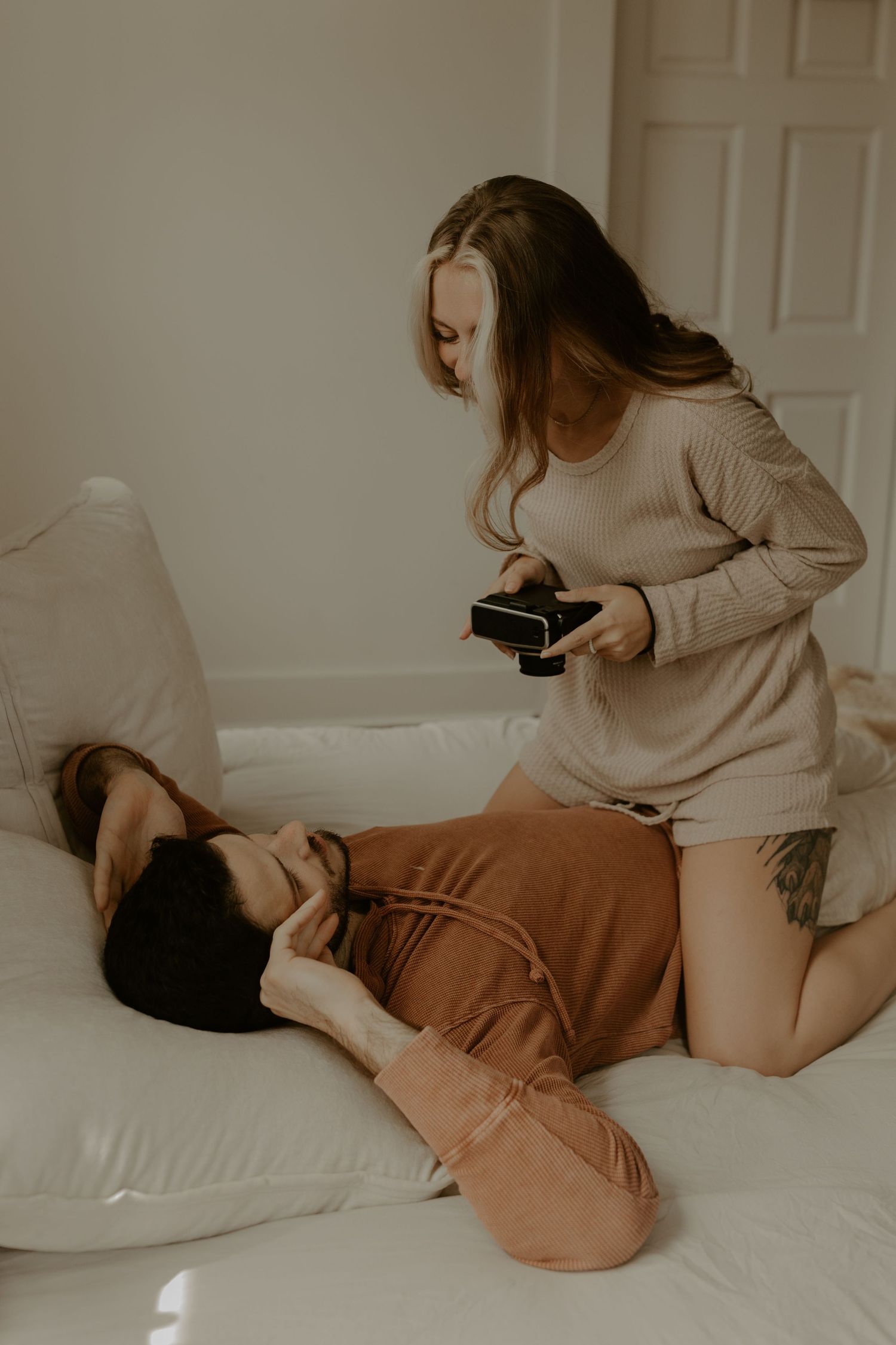 Candid moment of couple playing with camera on white couch.
