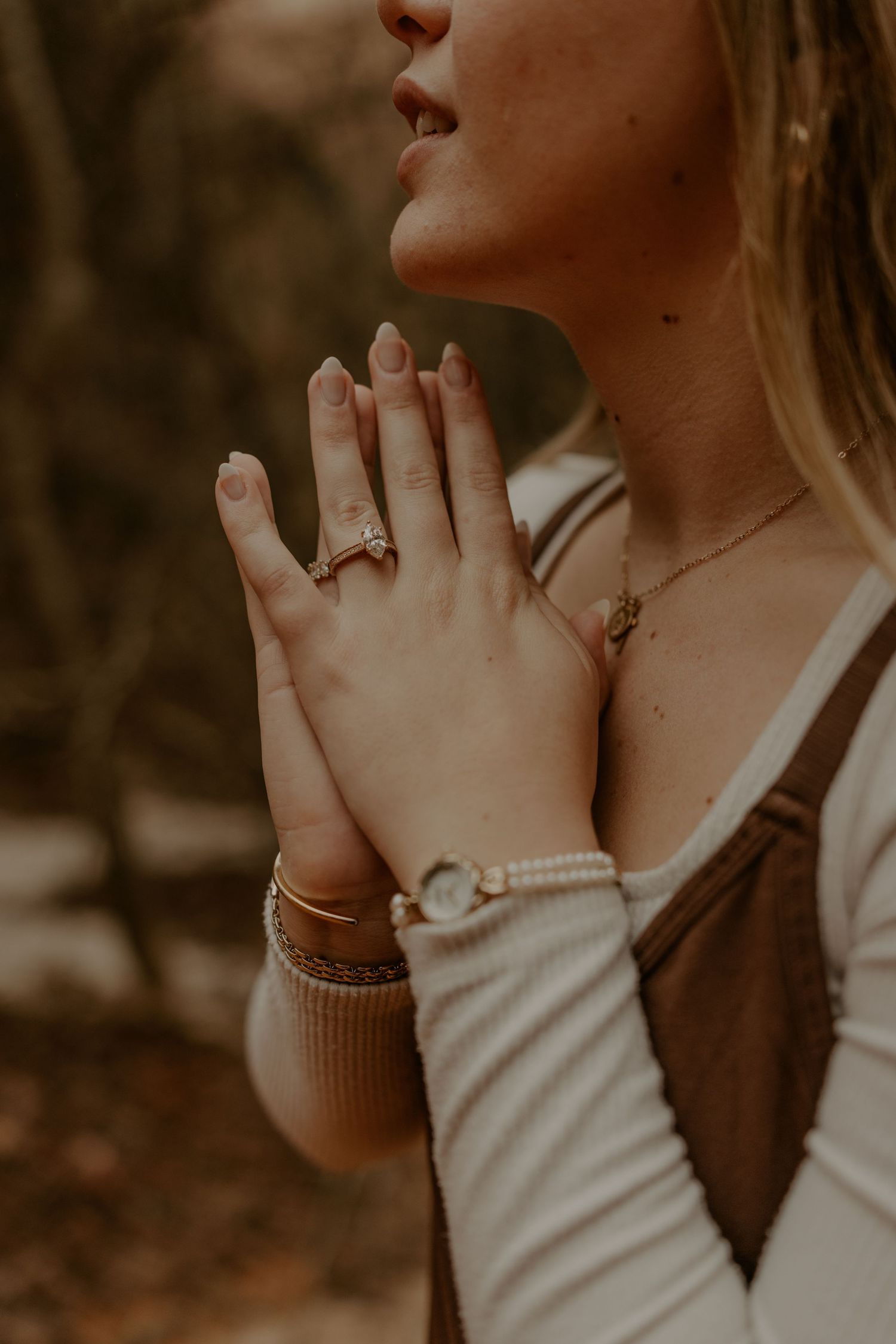 Close up of hands with engagement ring and jewelry in warm sunlight.
