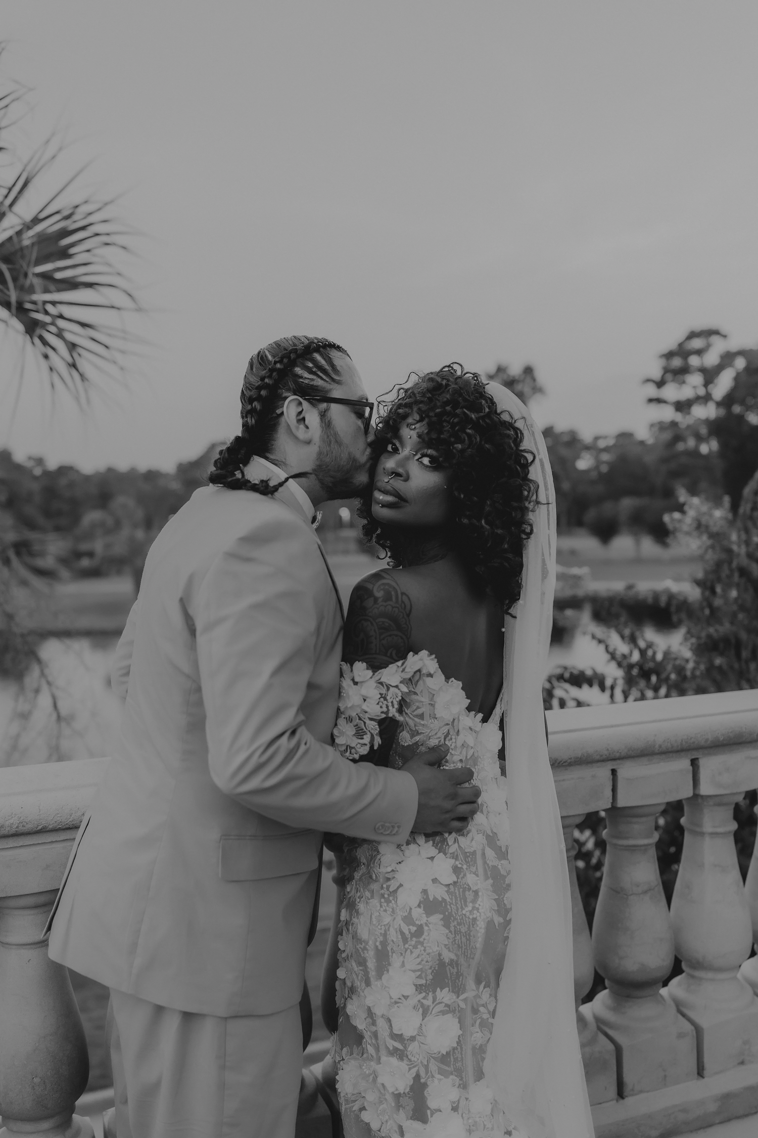 Wedding couple sharing tender moment on balcony with bride holding bouquet.