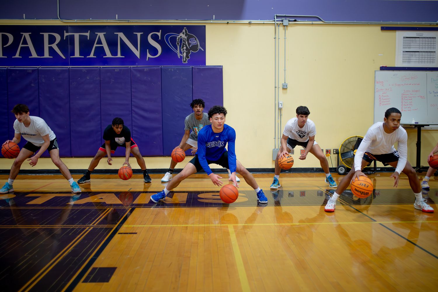 Wide shot of basketball players stretching and warming up in gymnasium with purple walls.