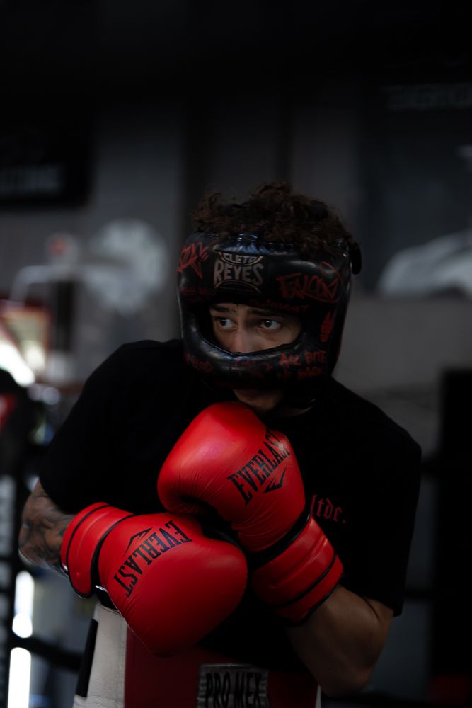 A boxer wearing protective headgear and red gloves poses in a fighting stance.