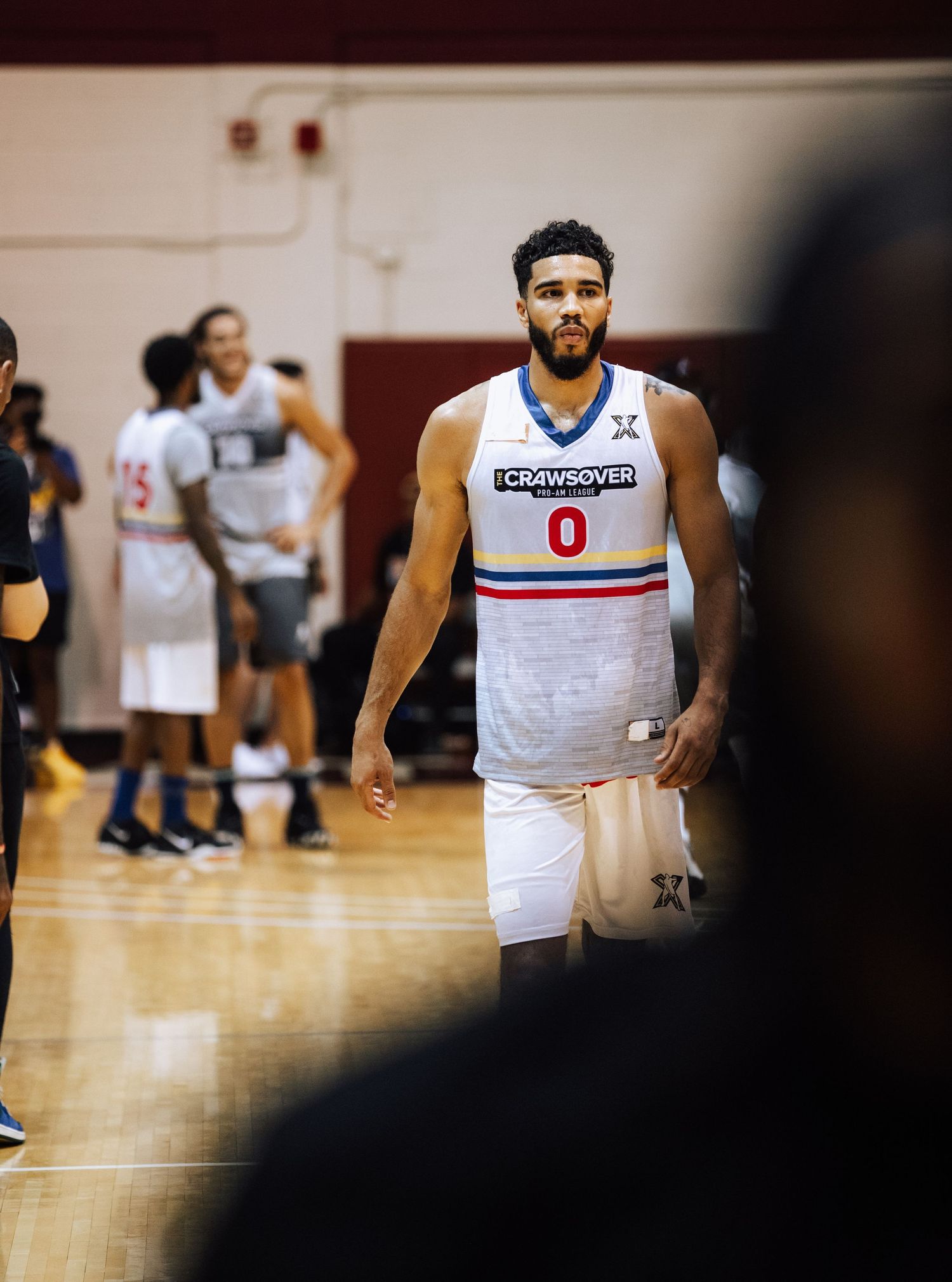 Basketball player wearing white jersey with number 0 stands on indoor court.