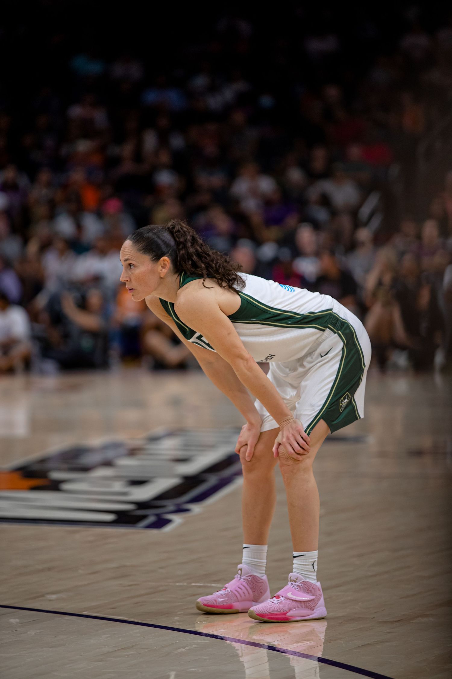 Professional basketball player in white and green uniform pauses during game wearing pink shoes on court.