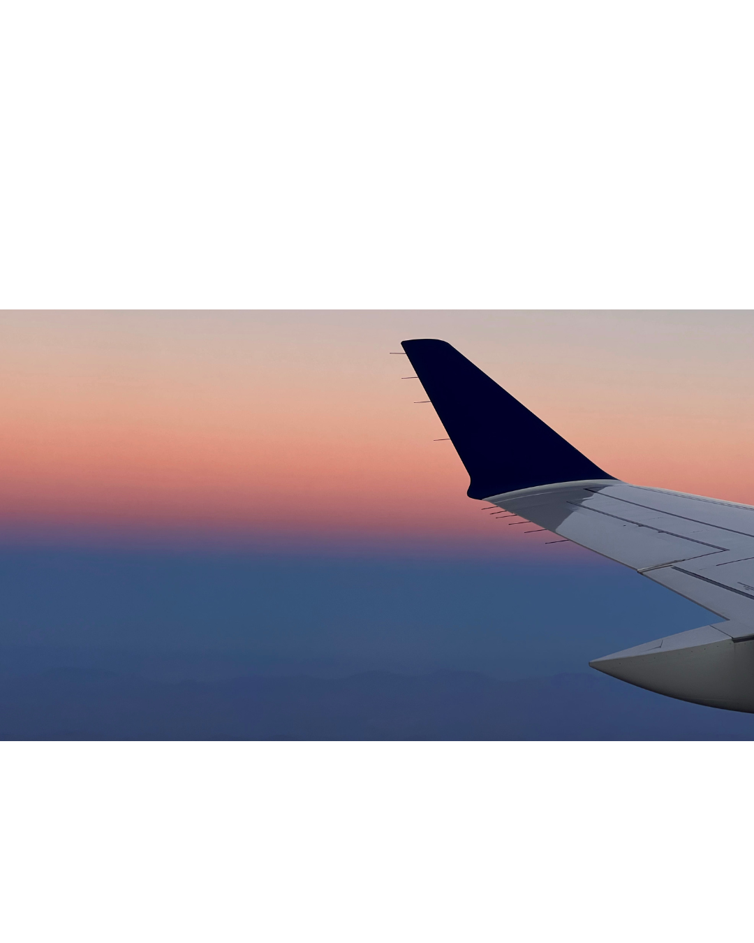 Aircraft wing silhouetted against a pink and blue sunset sky.