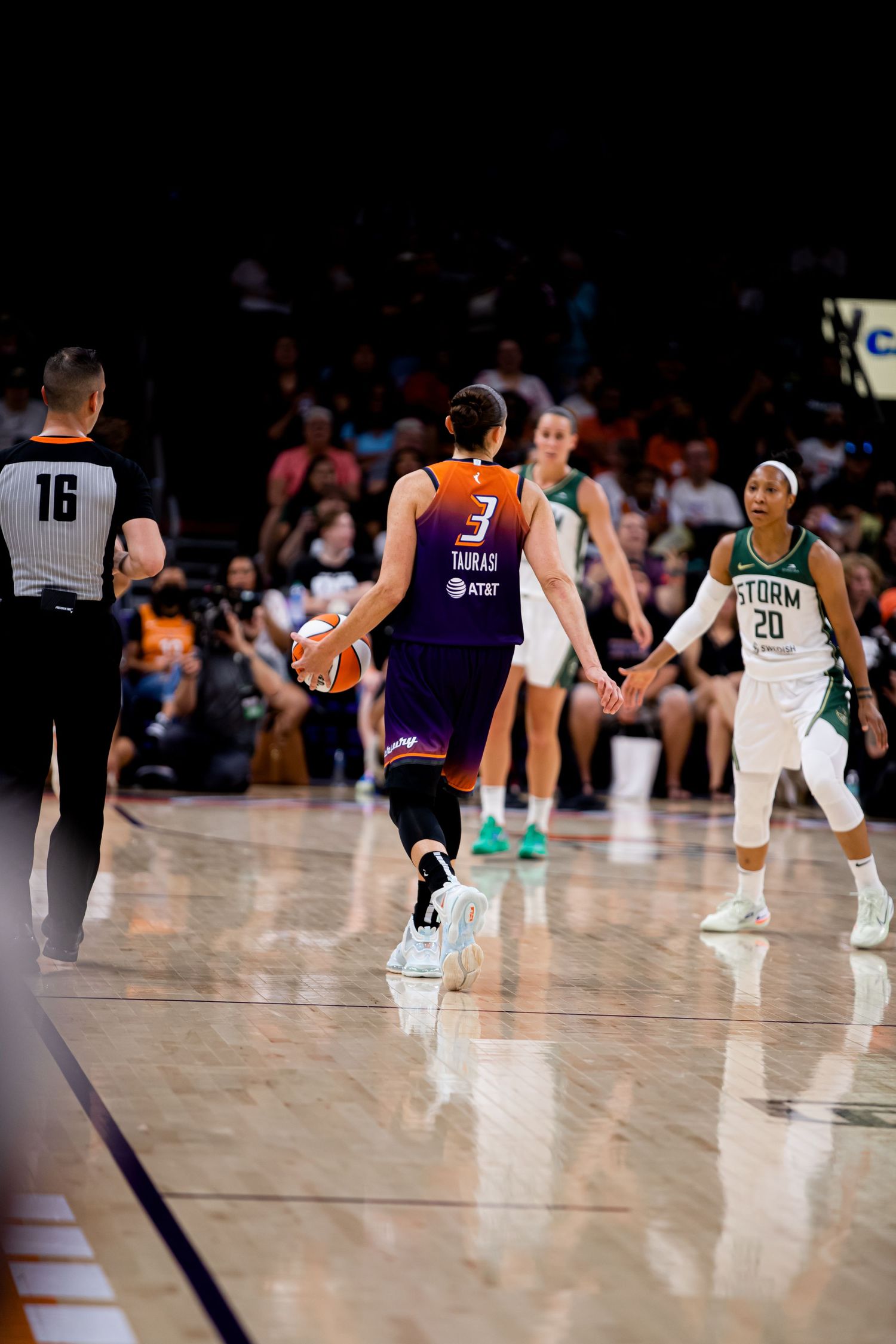 Basketball players and referee on court during professional game with reflective floor.