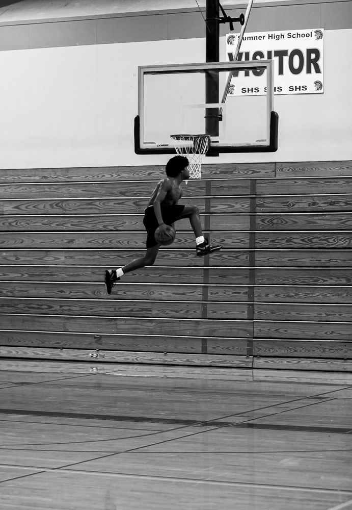 Player soars through air for layup under visitor scoreboard in black and white photo.