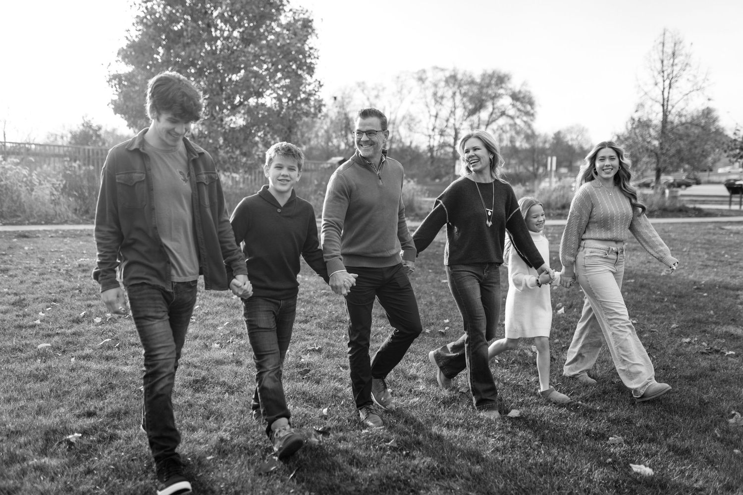 A small group holding hands and walking together through a grassy park in black and white.