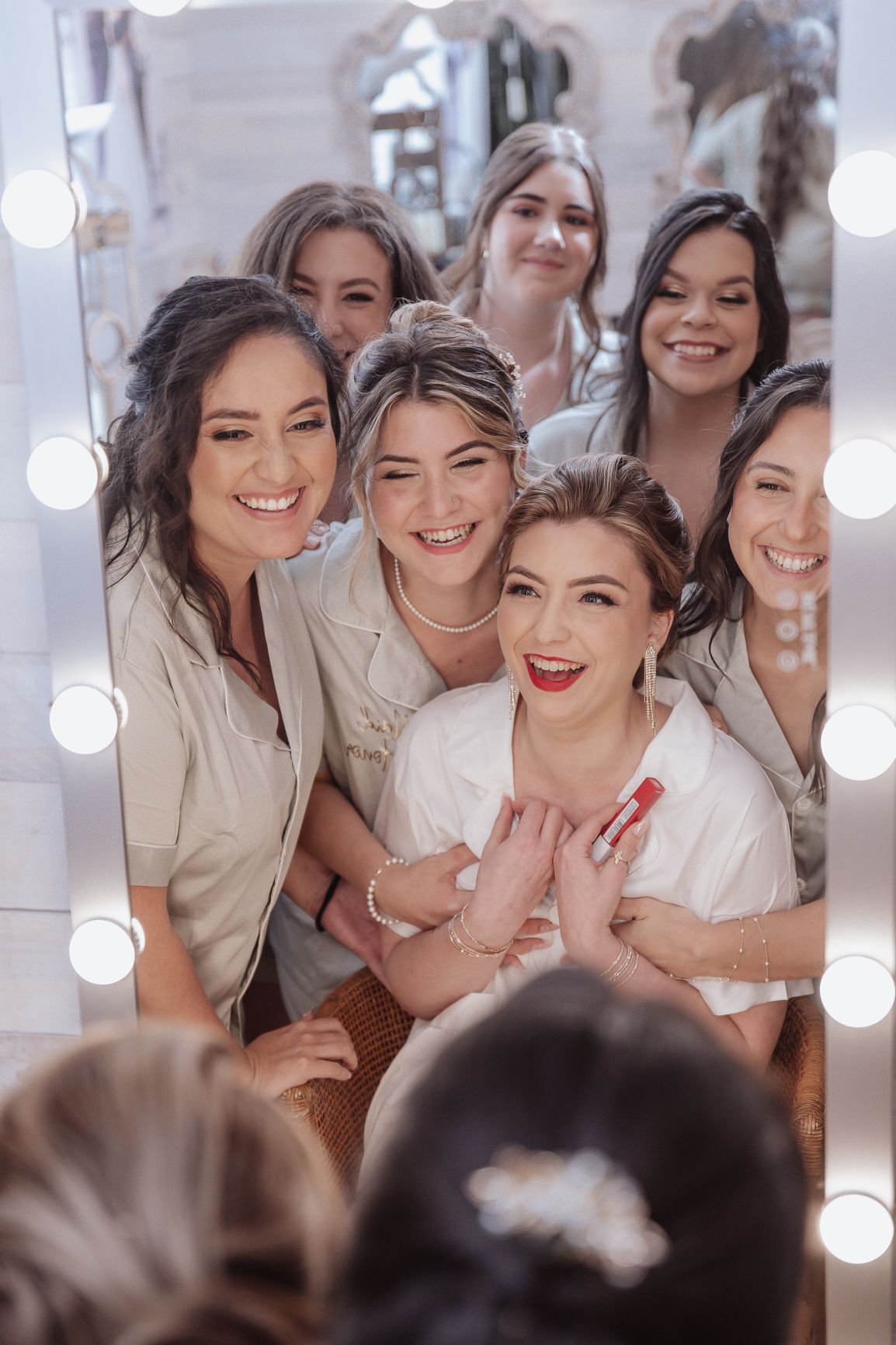 Happy group of women posing and laughing together in front of makeup mirror.