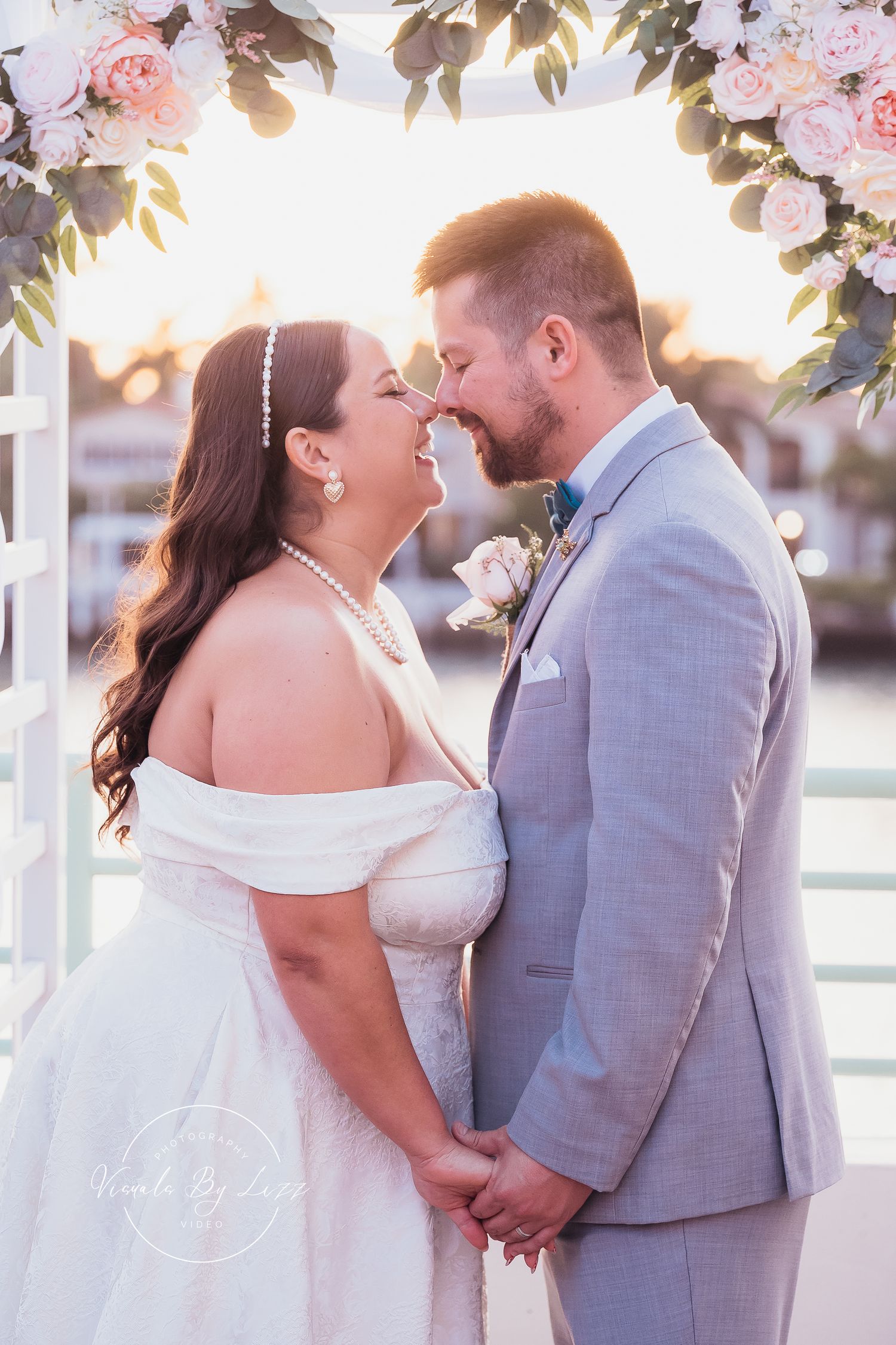 Sunset wedding portraits under floral arch with couple in white dress and grey suit.