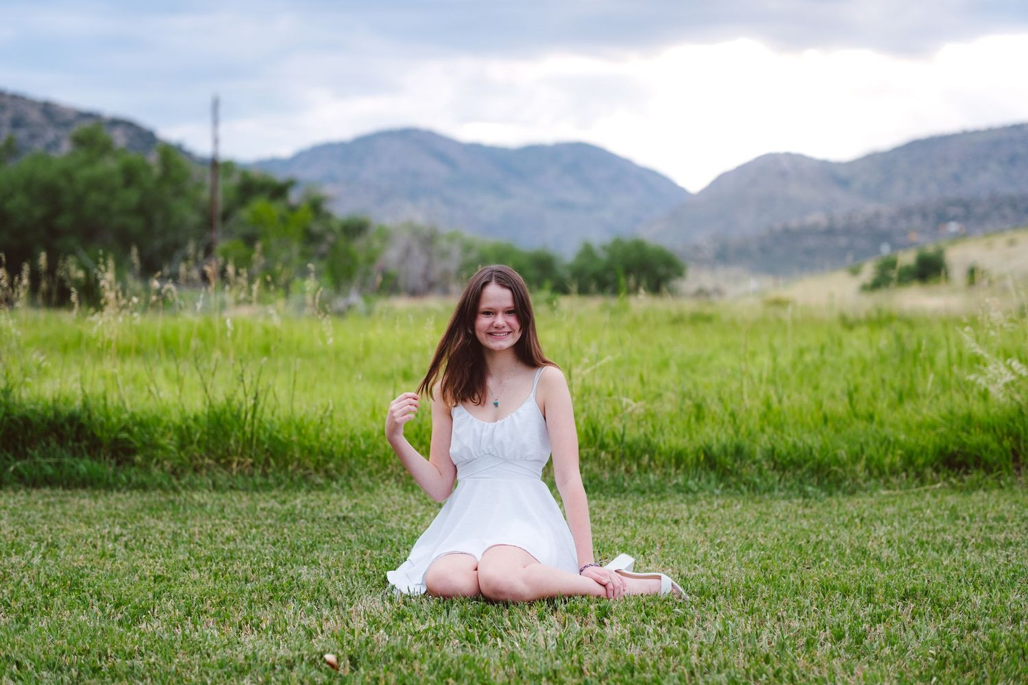 Teen girl sitting in green field, mountains in background.