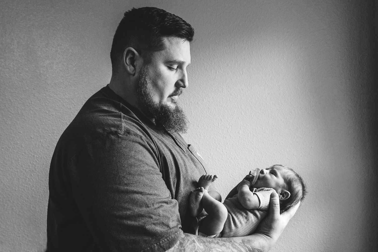 Profile of father holding tiny baby boy in his arms, father looking down with calm expression.
