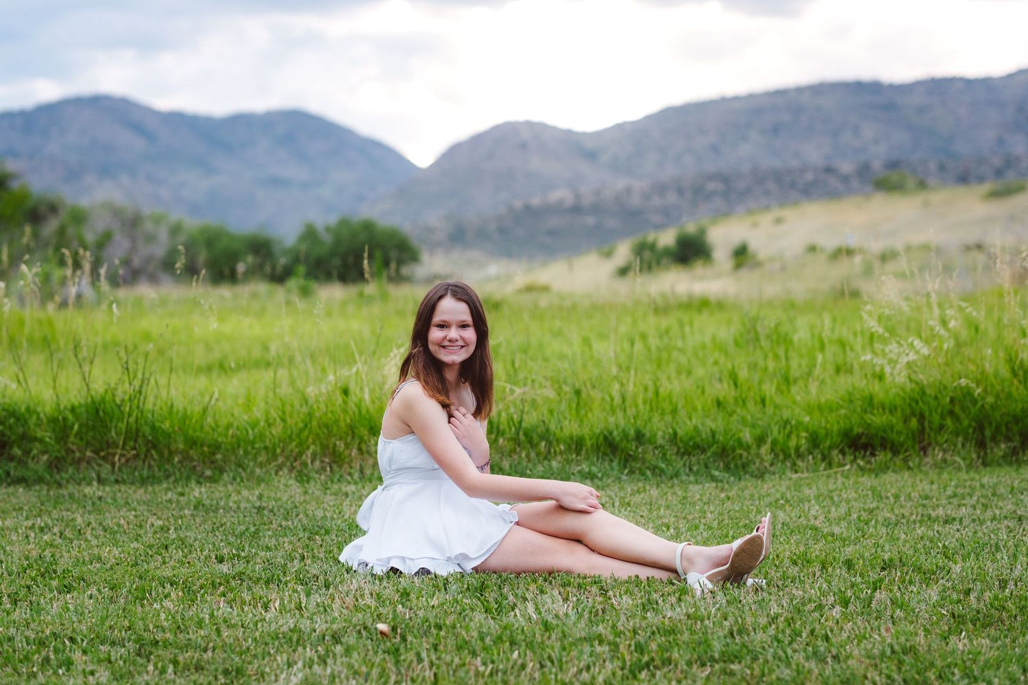 Teen girl sitting in green field, foothills in background.