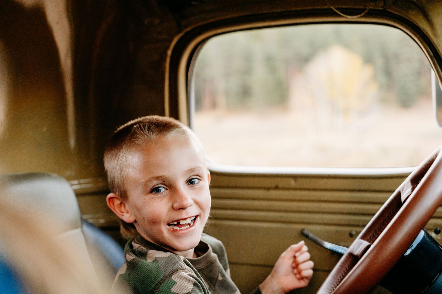 Young boy smiling inside vintage green truck.