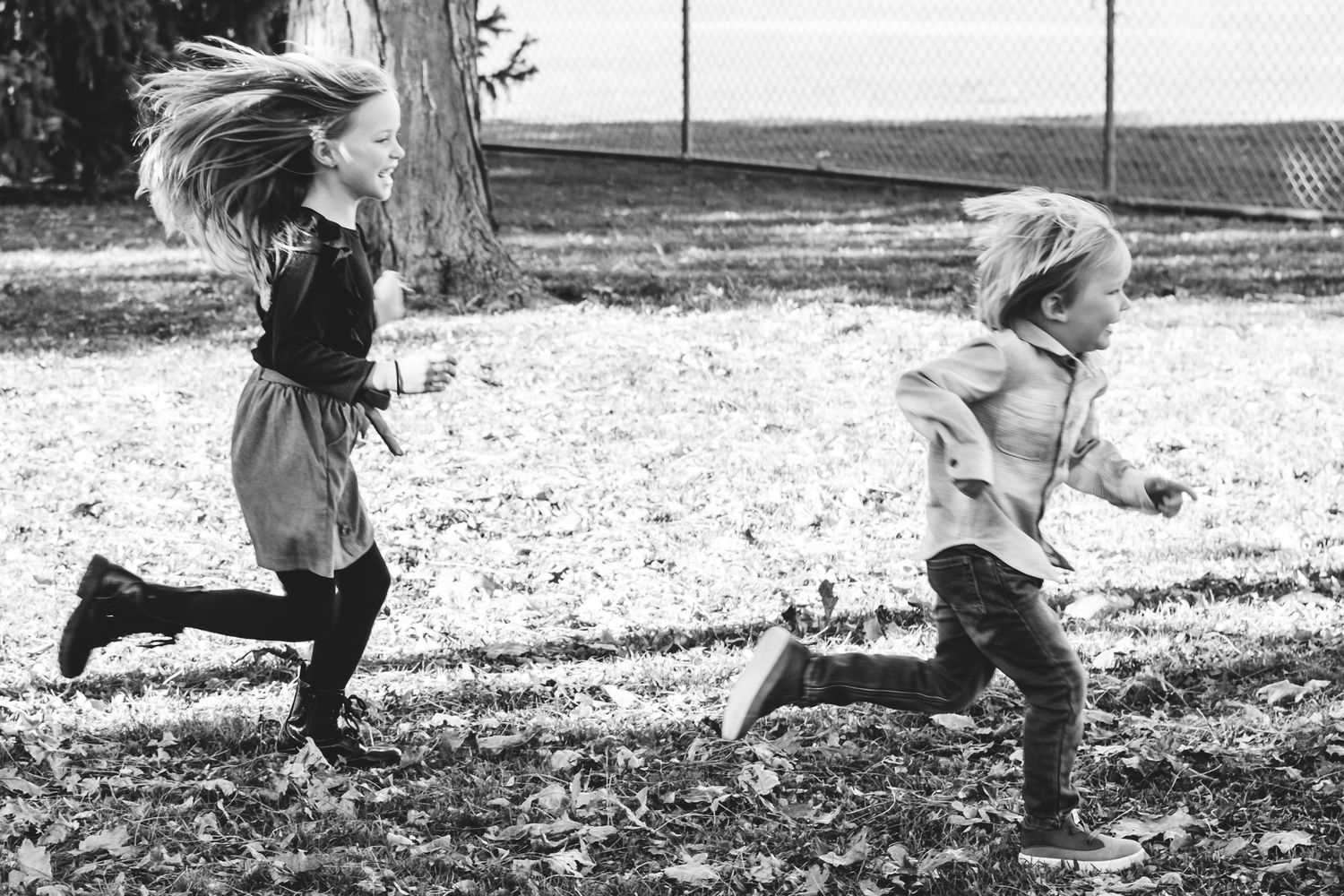 Black and white candid portrait of profile two young children running in park.