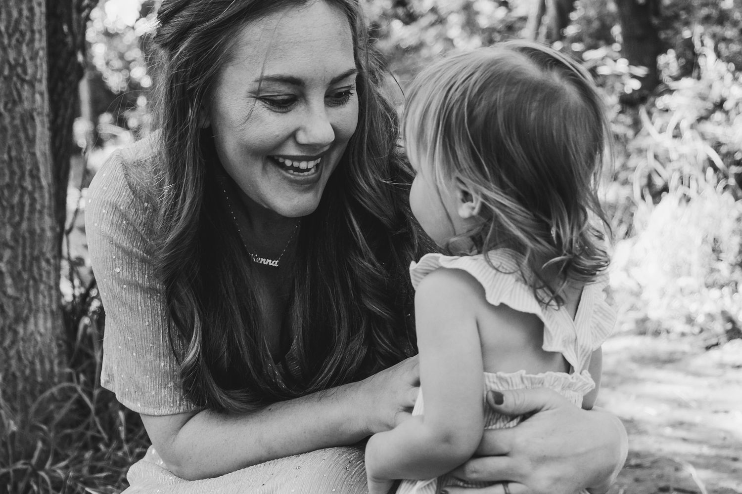 Mother kneeling down at toddler daughter's level, smiling while wrapping arms around her daughter.