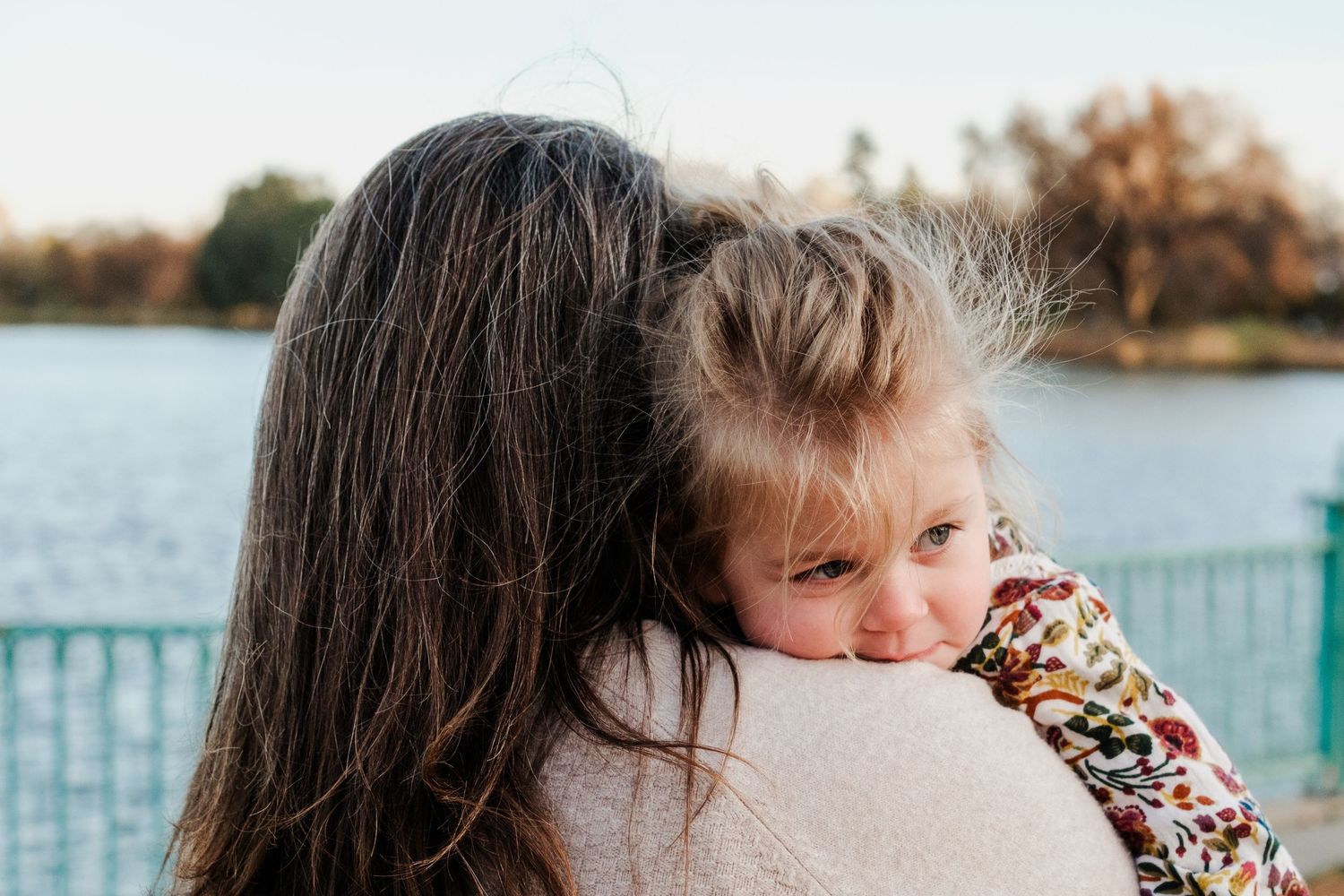 Toddler daughter resting on mother's shoulder, Ferrill lake and teal fencing in the background