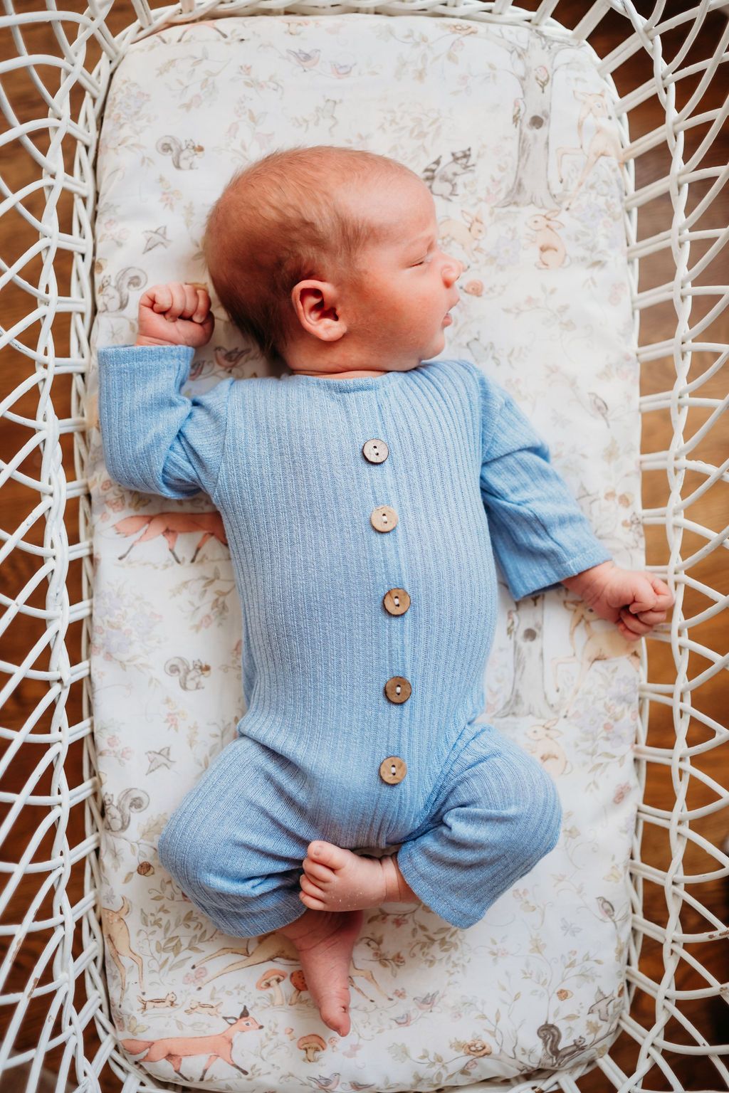 Overhead view of newborn baby boy dressed in blue sleeping in bassinet.