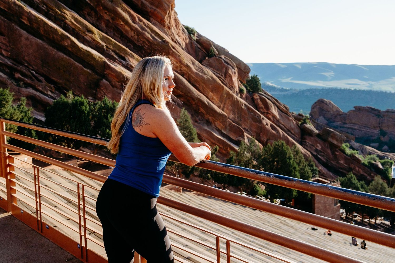 Fitness branding photography with female trainer leaning on railing atop Red Rocks.