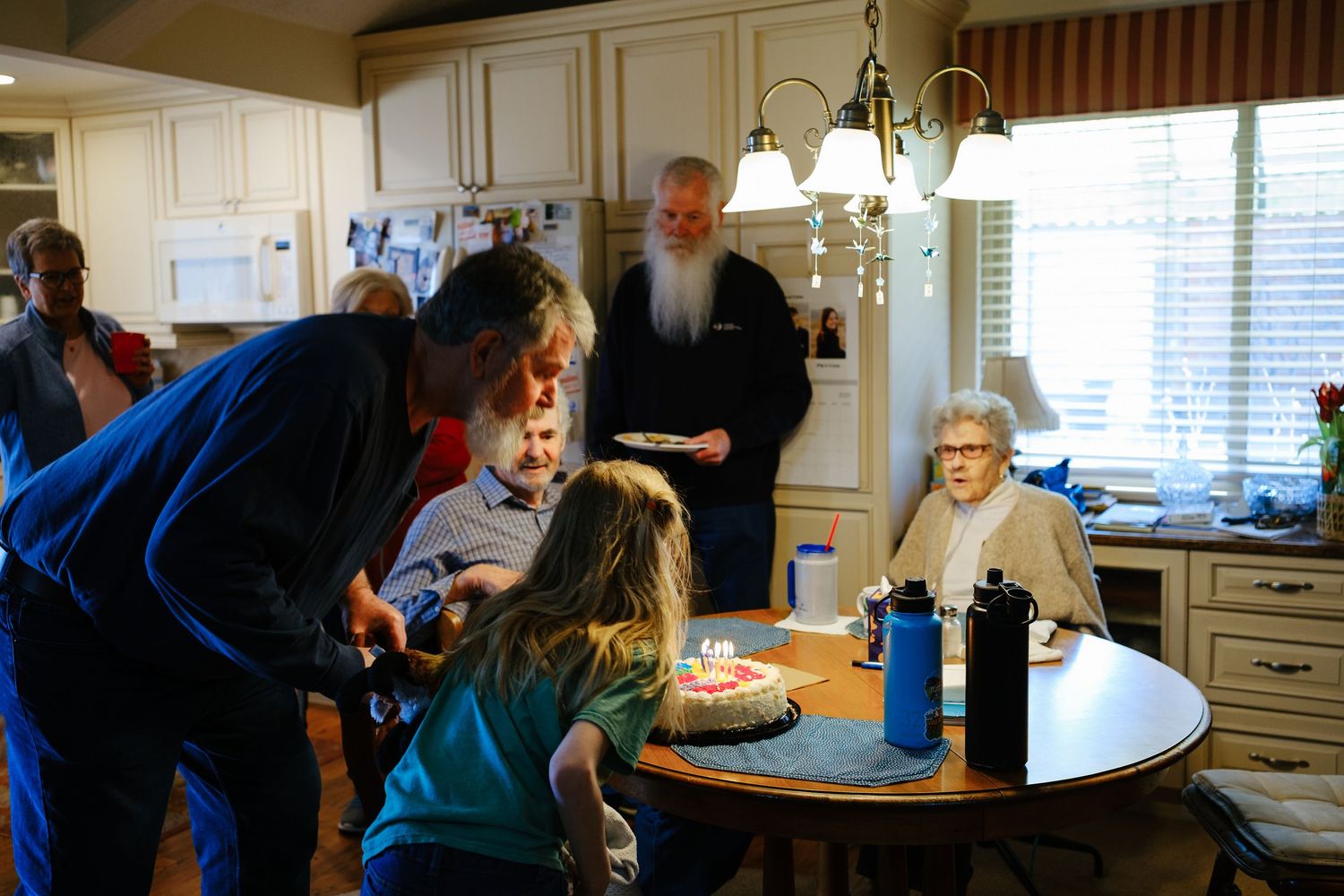 Multi generation family photo of grandfather blowing out candles on his birthday.