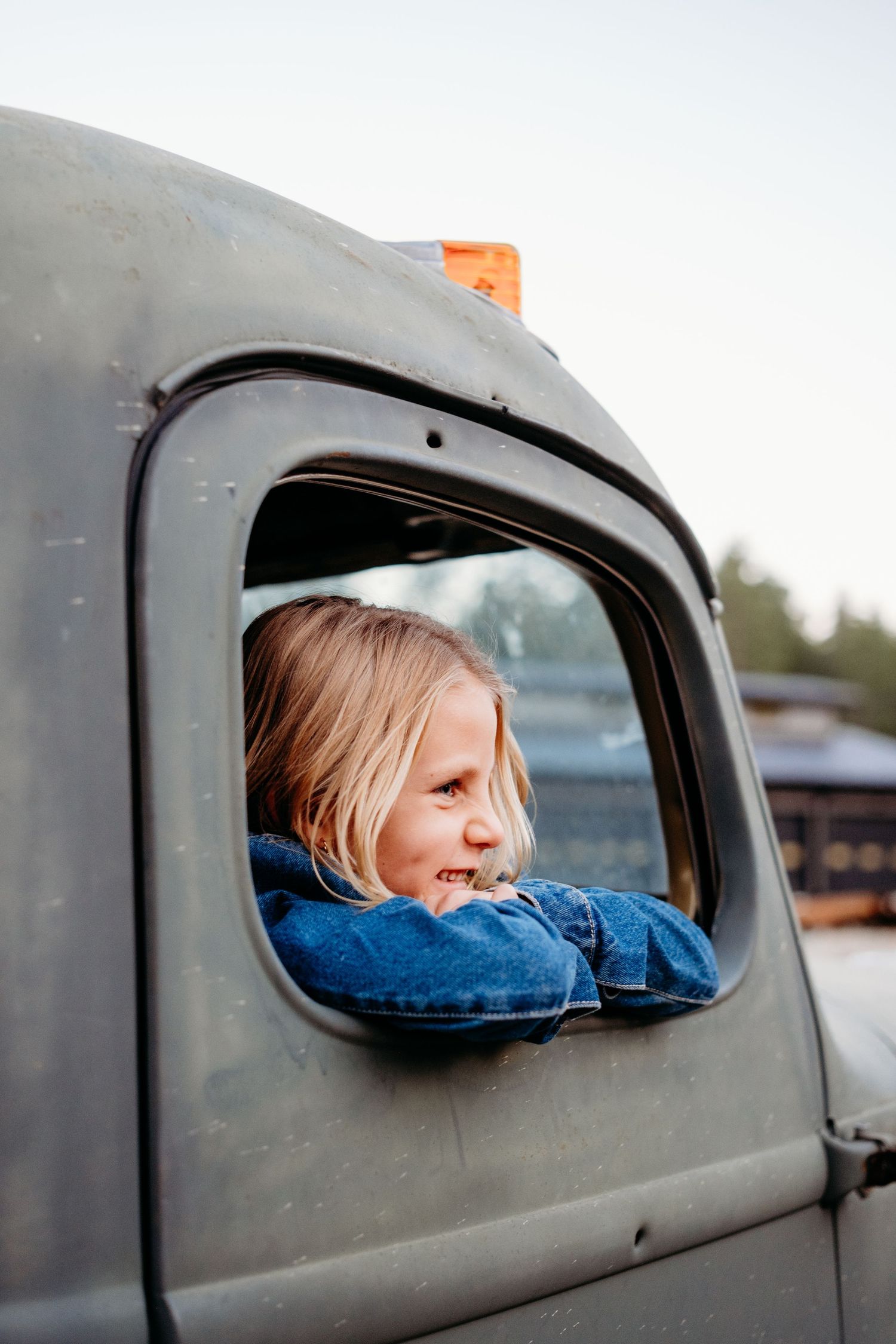 Young girl resting arms on the window sill of a vintage green truck, looking off into the distance.