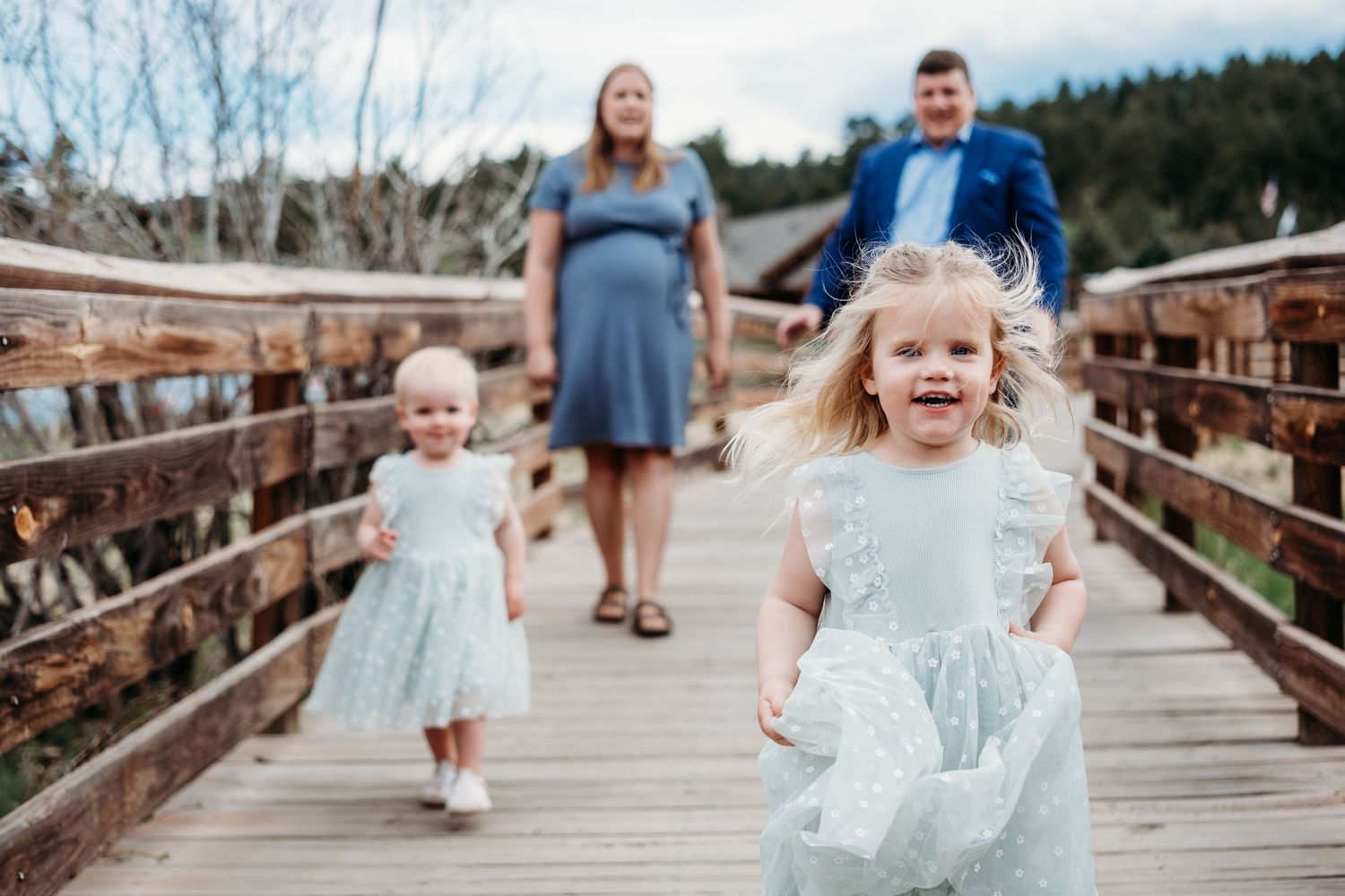 Family walking on wooden boardwalk in Evergreen, toddler girl in foreground smiling.