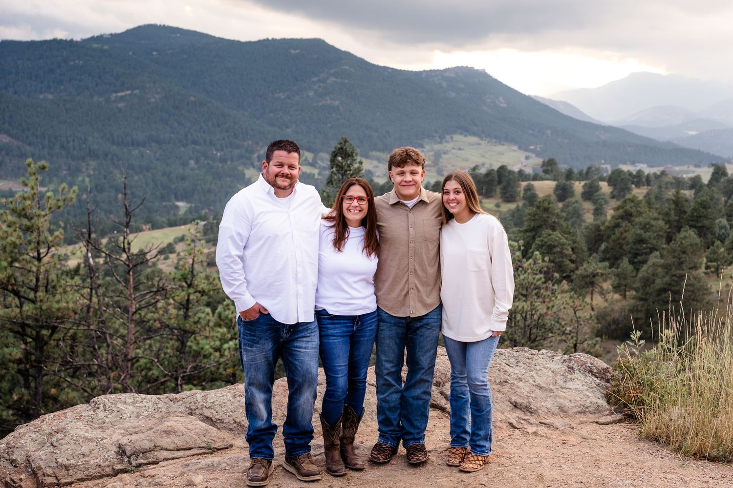 Father, mother, son and son's girlfriend all standing on rocky overlook at Mount Falcon West, mountains and moody skies in background.