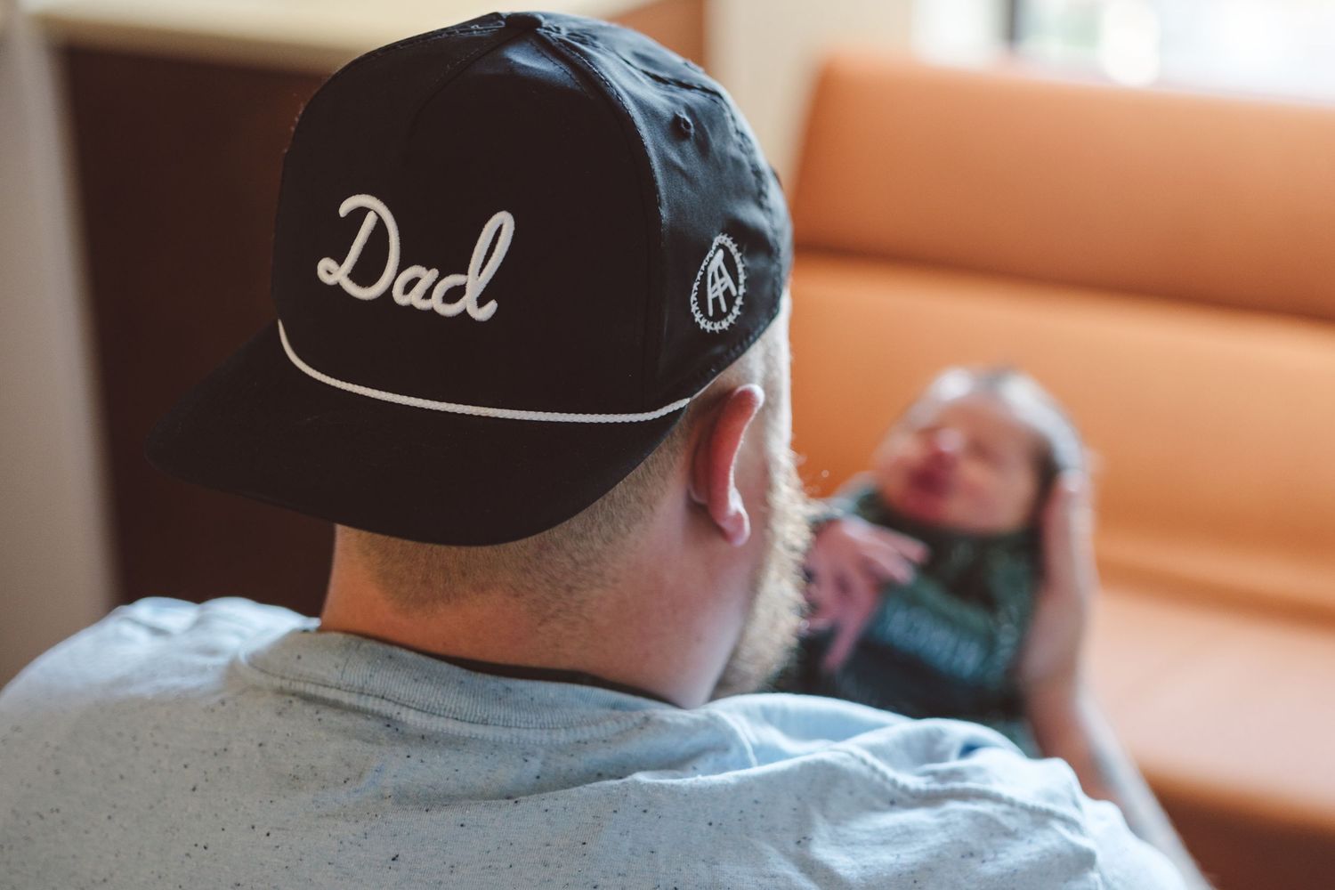 Father holding newborn, wearing a hat that reads
