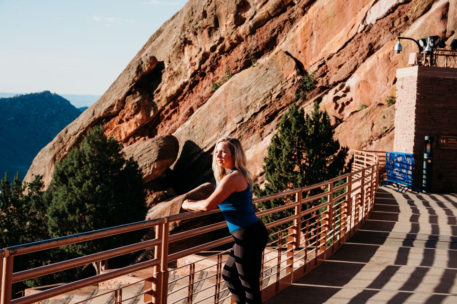 Female trainer standing atop Red Rocks Amphitheater, leaning against rail, looking off into distance.