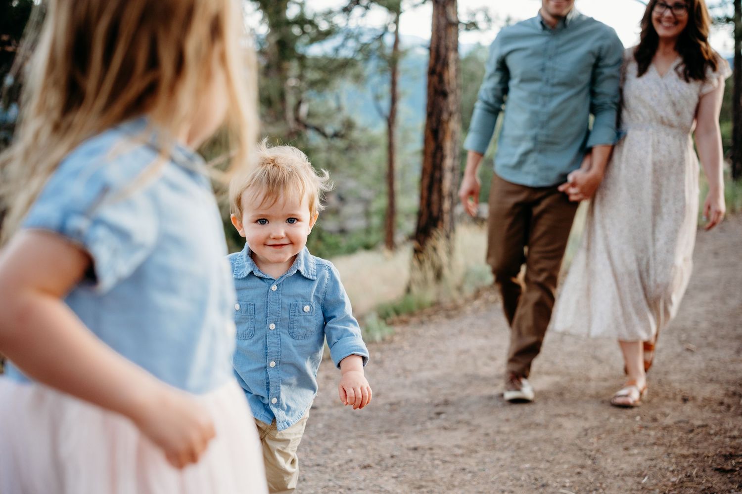 Daughter blurred in foreground, son walking in middle ground, parents following behind in foreground, all walking dirt path at Mount Falcon.