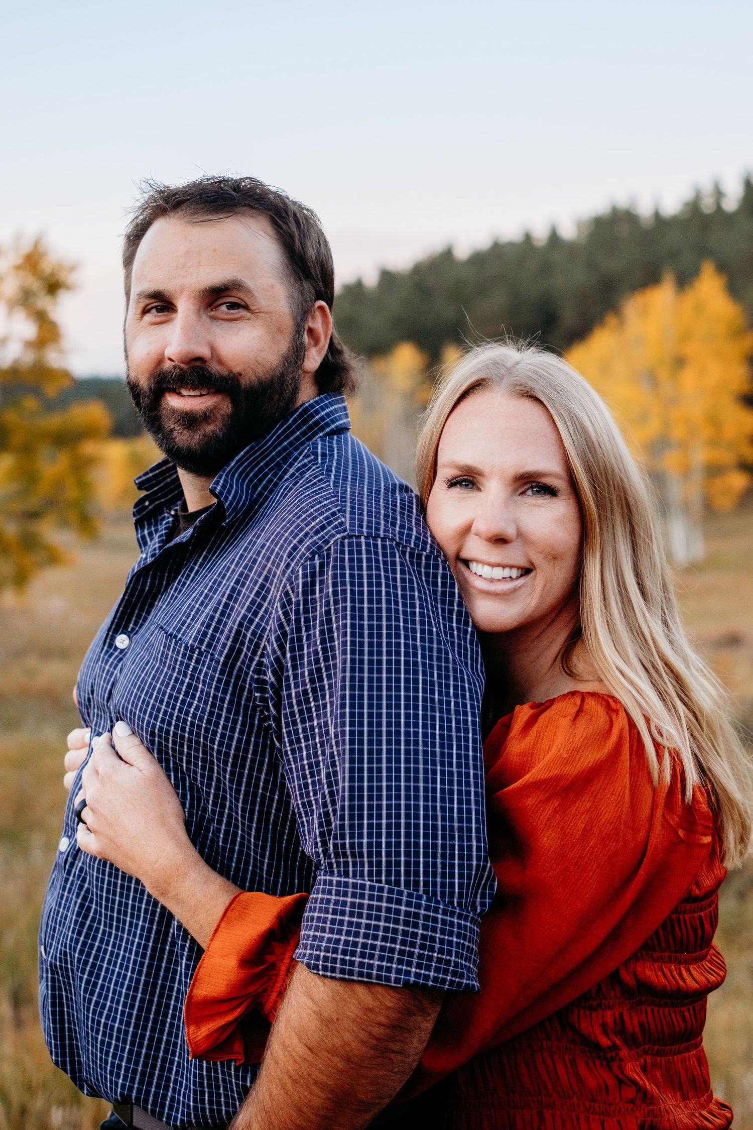 Husband and wife standing together in Evergreen, fall colored aspen trees in the background.