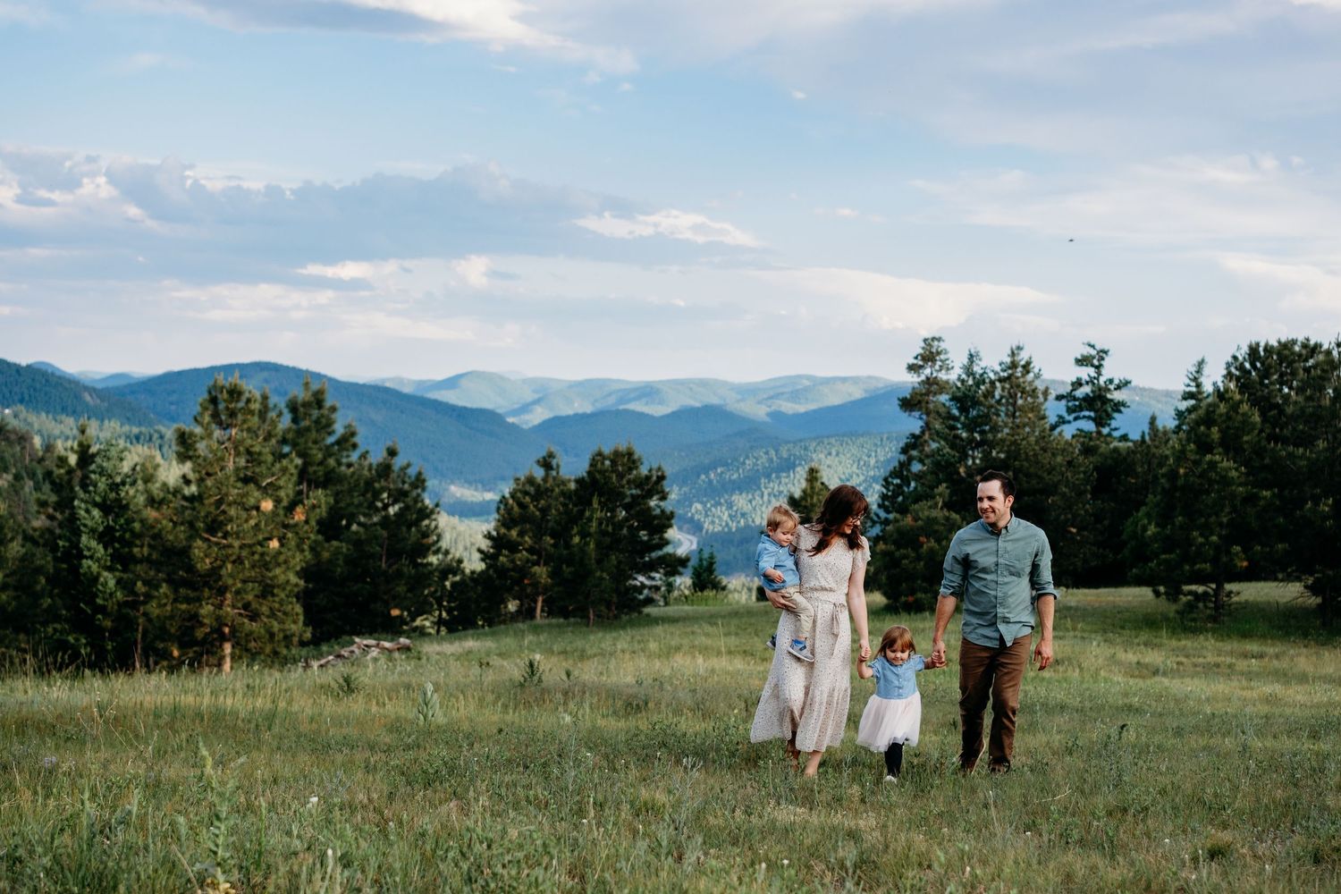 Father and mother, holding toddler son, walking on each side of their young daughter, breathtaking mountain views at Mt Falcon West.