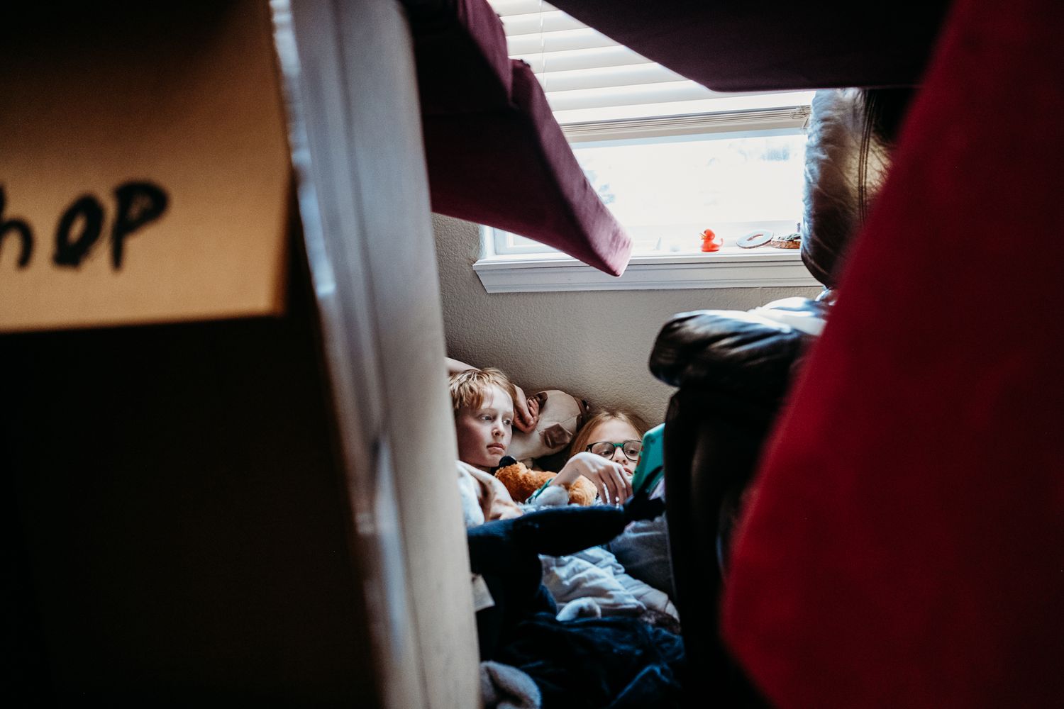 Kids watching on device inside fort made of boxes.