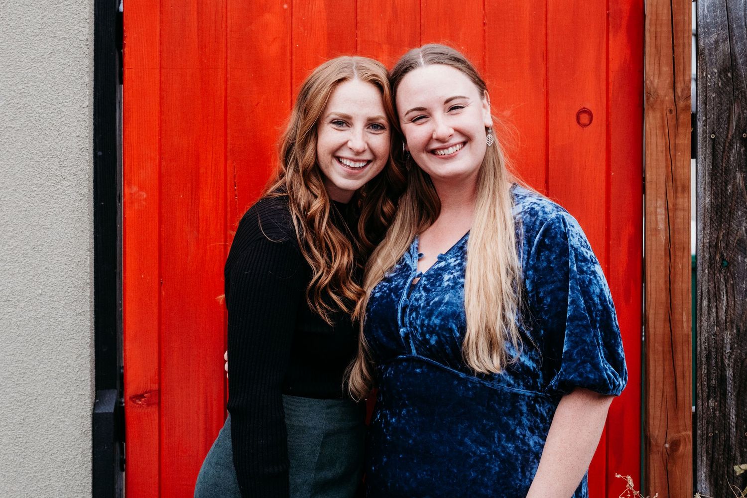 Adult sisters standing close together in front of orange-red door in Denver, CO